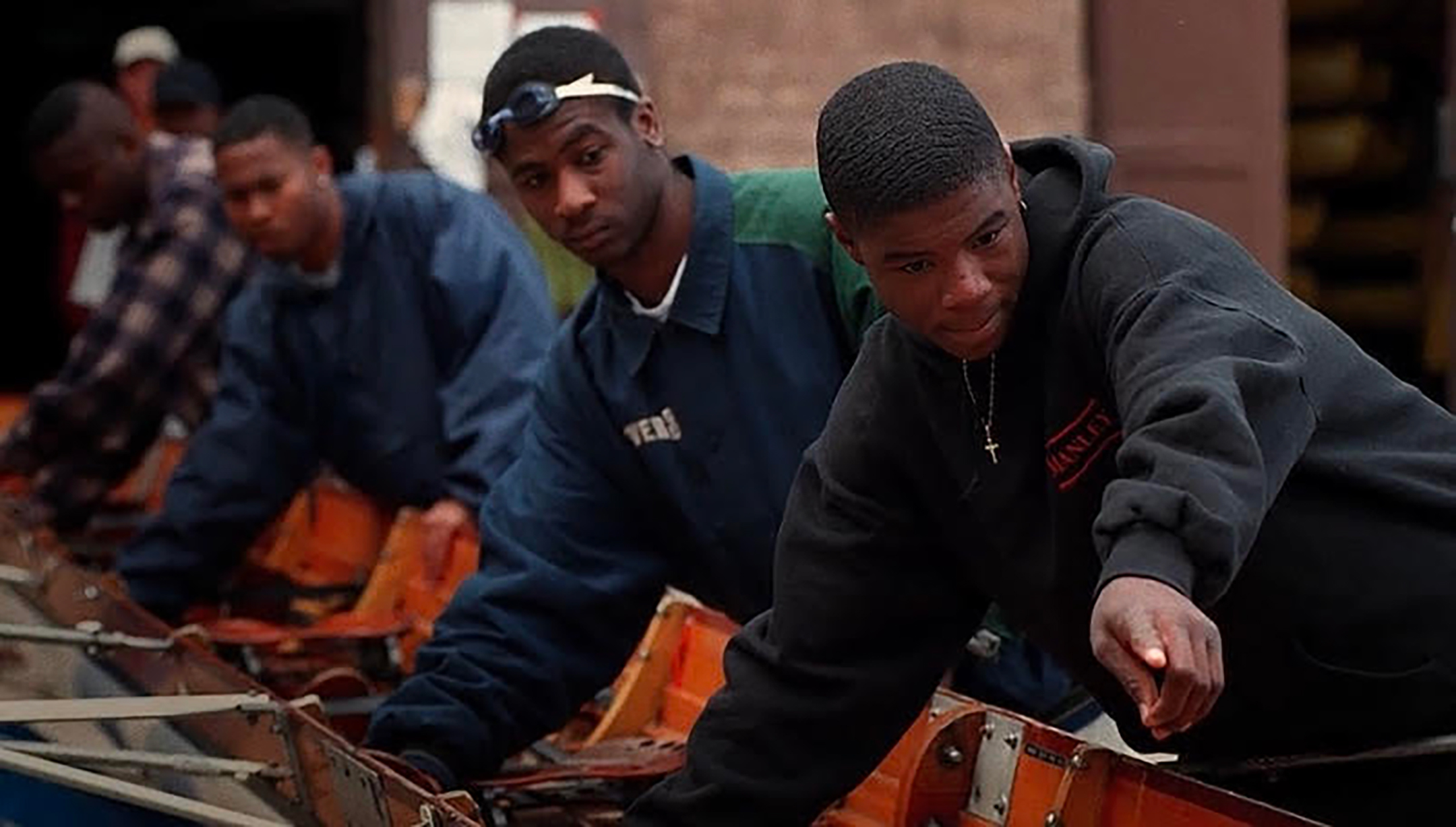 A group of young black men work on a boat for their crew team