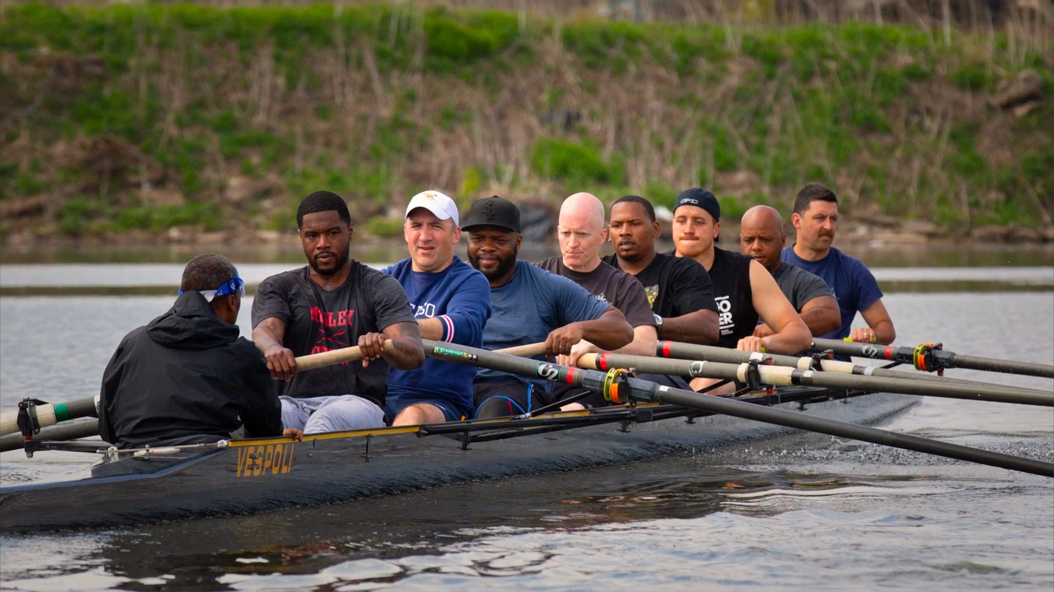 nine people in a boat, five black and four white, rowing on a river