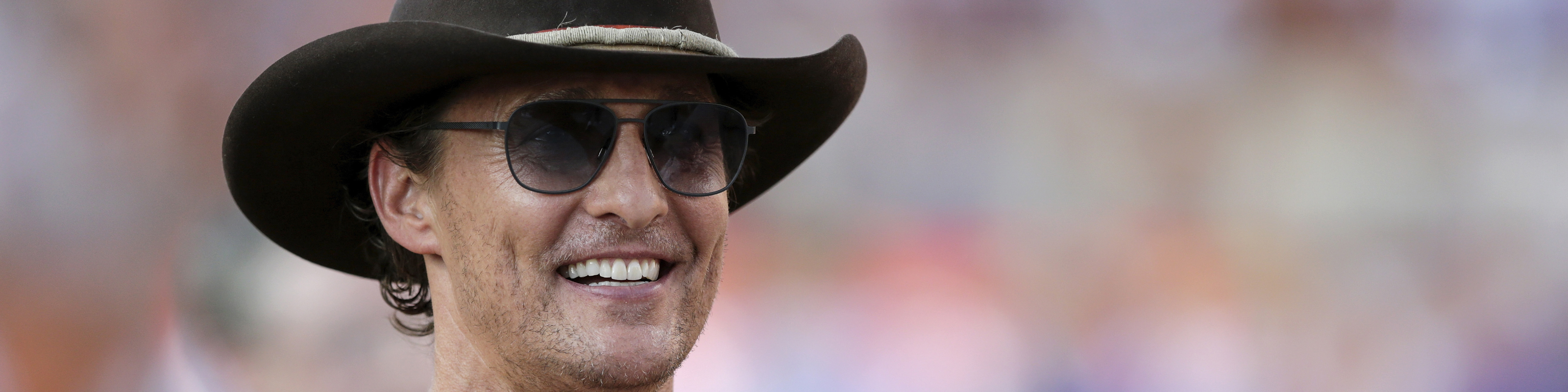 a photo of actor Matthew McConaughey wearing a dark cowboy hat and sunglasses and smiling broadly
