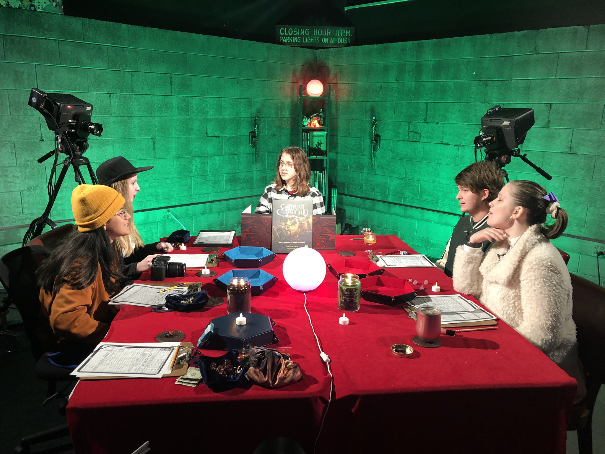 five of teacher bill allan's students play a game of dungeons and dragons on a video set with a red table and walls with green light