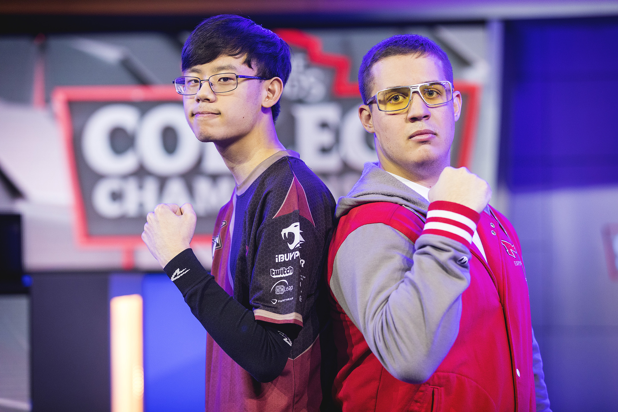 two male college e sports competitors pose standing back to back on a stage