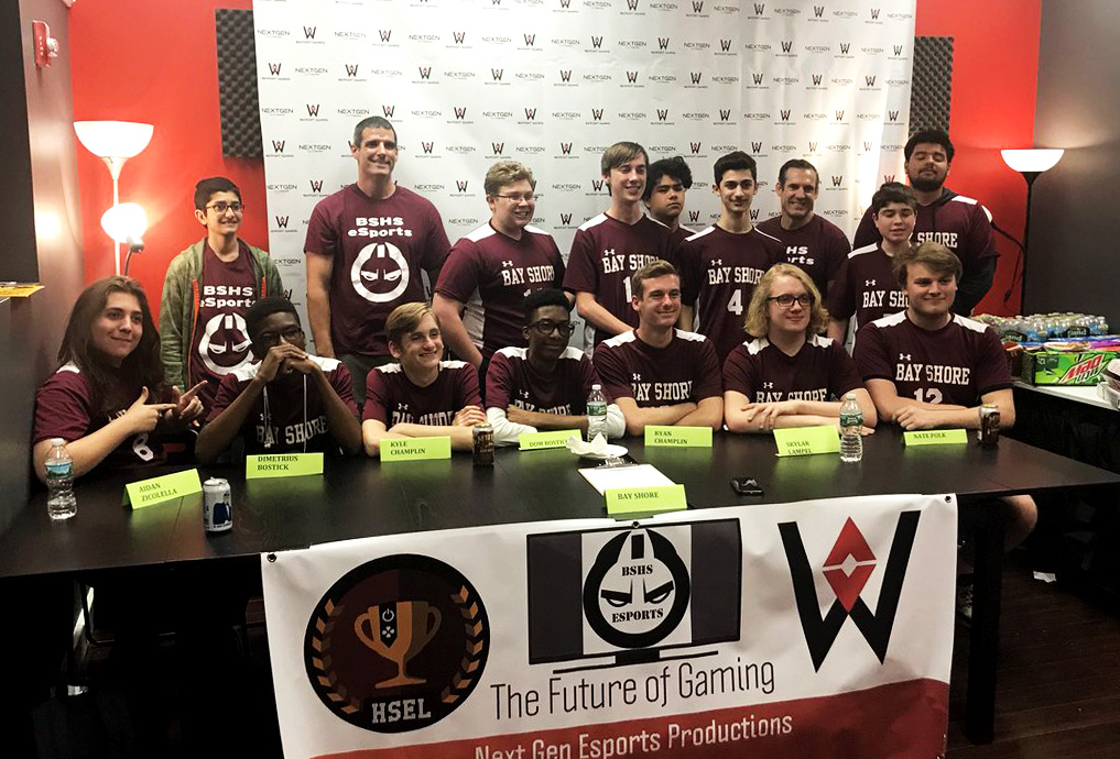 male and female members of the bay shore e sports team pose for a photo with some seated at a table and others standing behind them