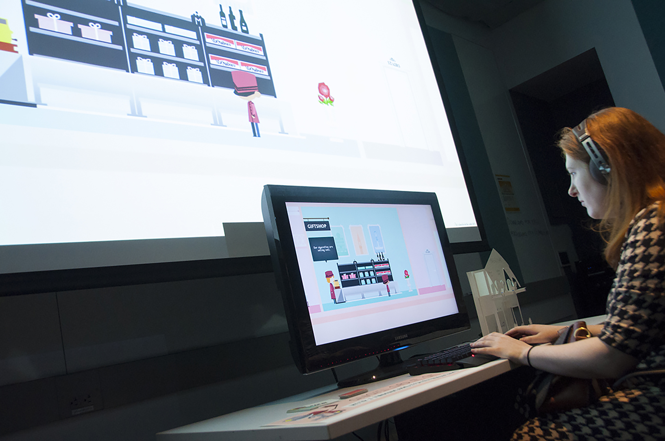 A female student sits in front of a large screen and works on a laptop programming at game at the NYU Game Center Incubator