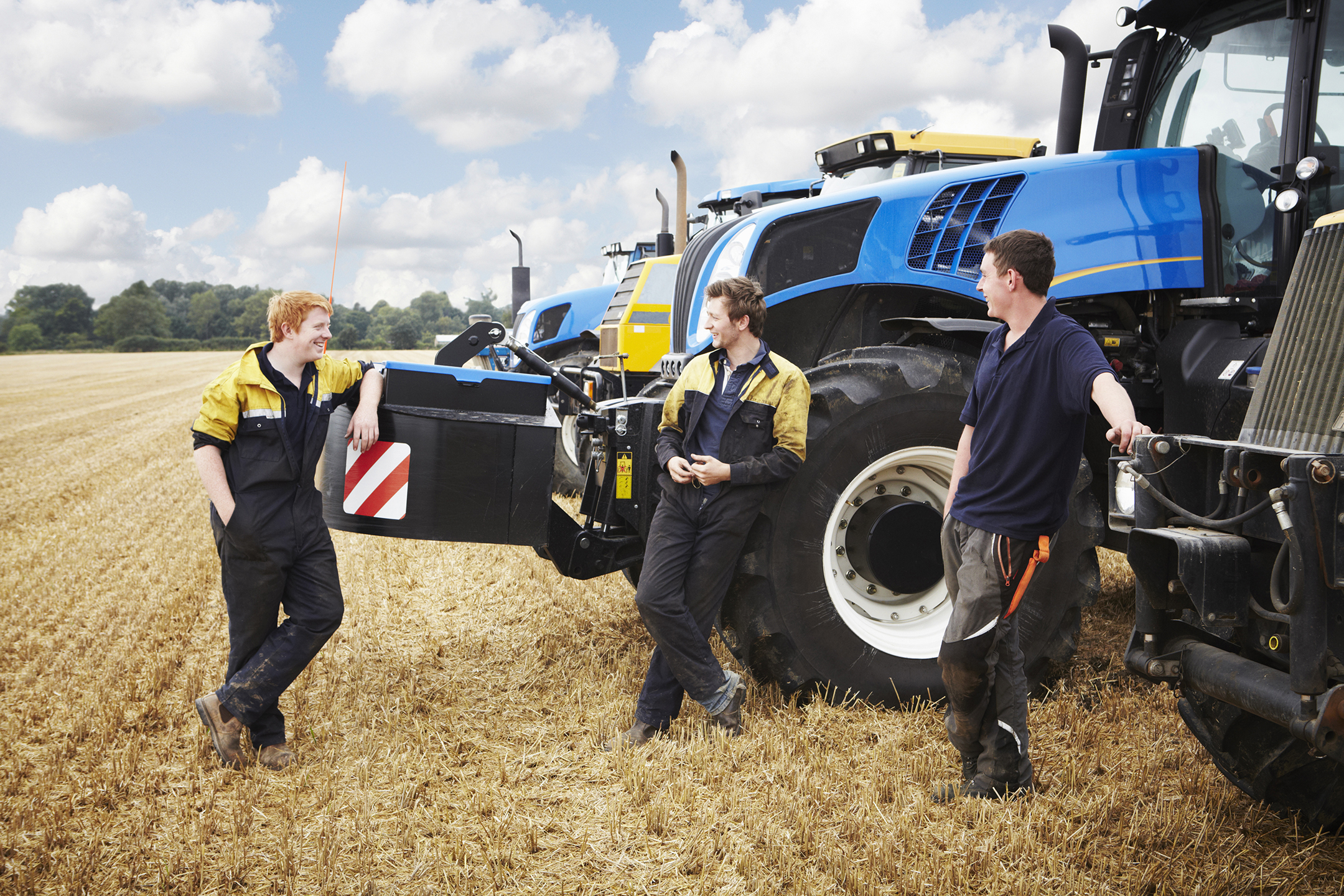 three young men chatting and laughing as they stand next to tractors parked on farmland