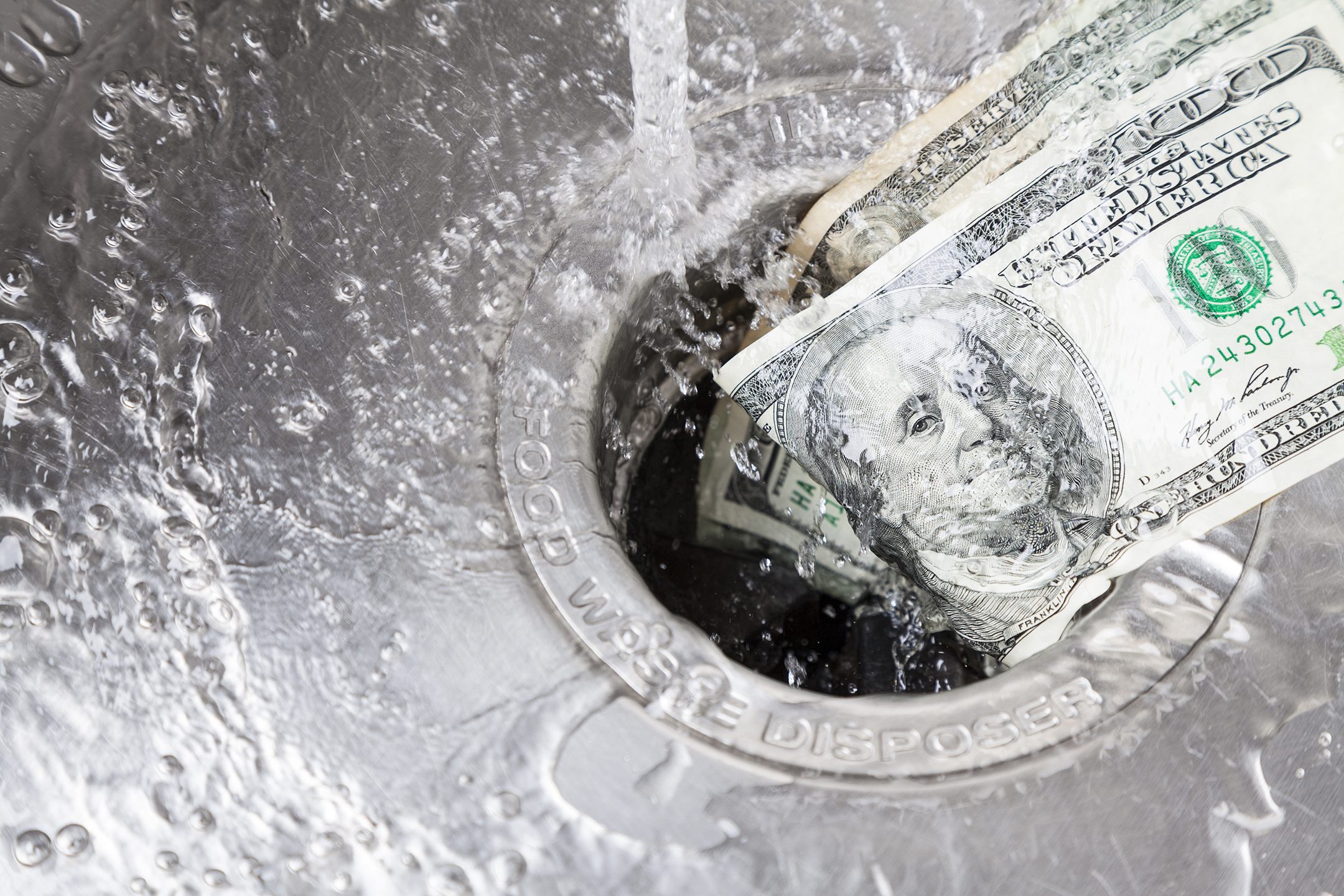 water running down a kitchen sink drain that is stuffed with hundred dollar bills
