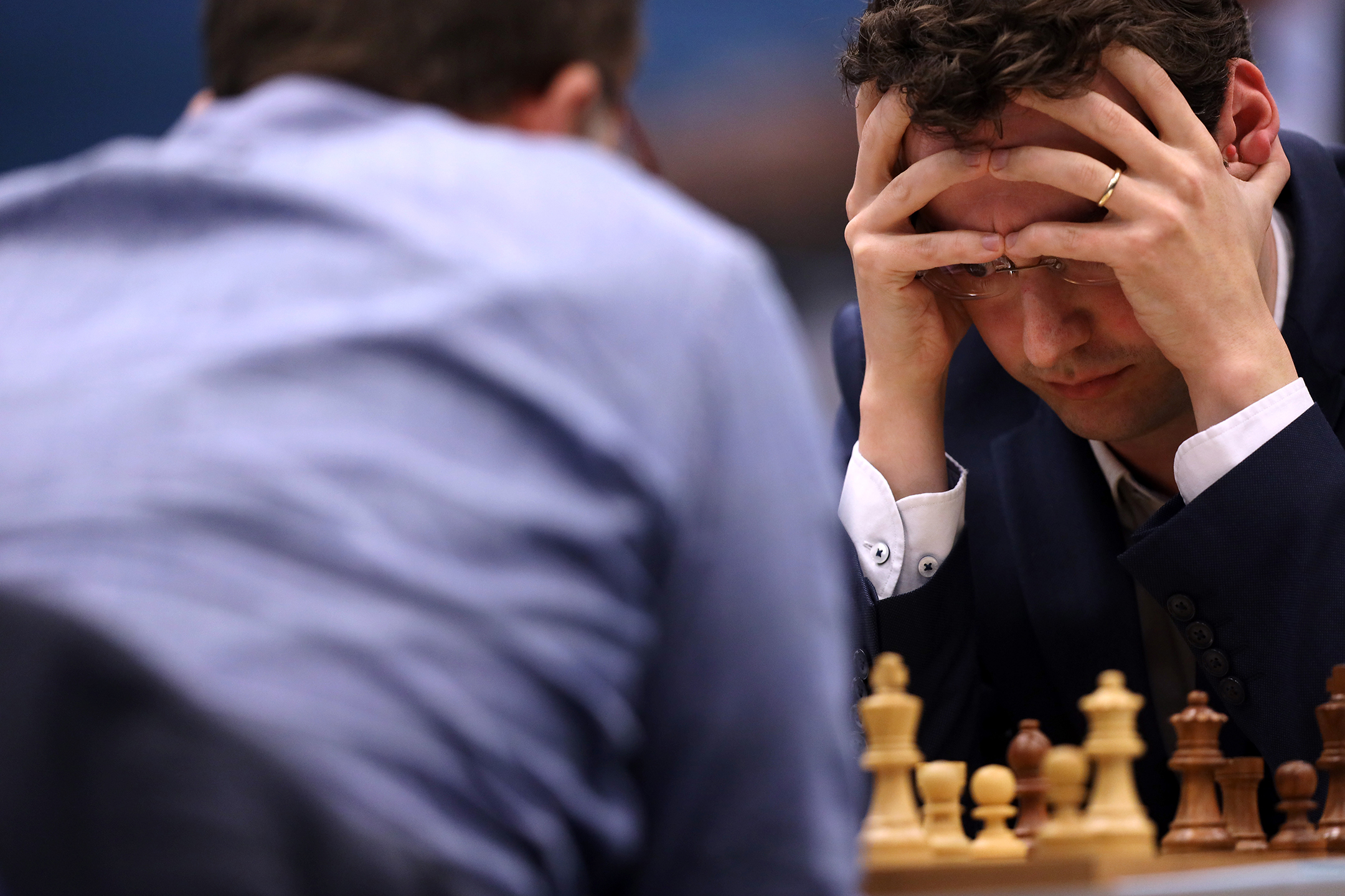two men play chess, with one of them holding his head in his hands as he concentrates on making a move