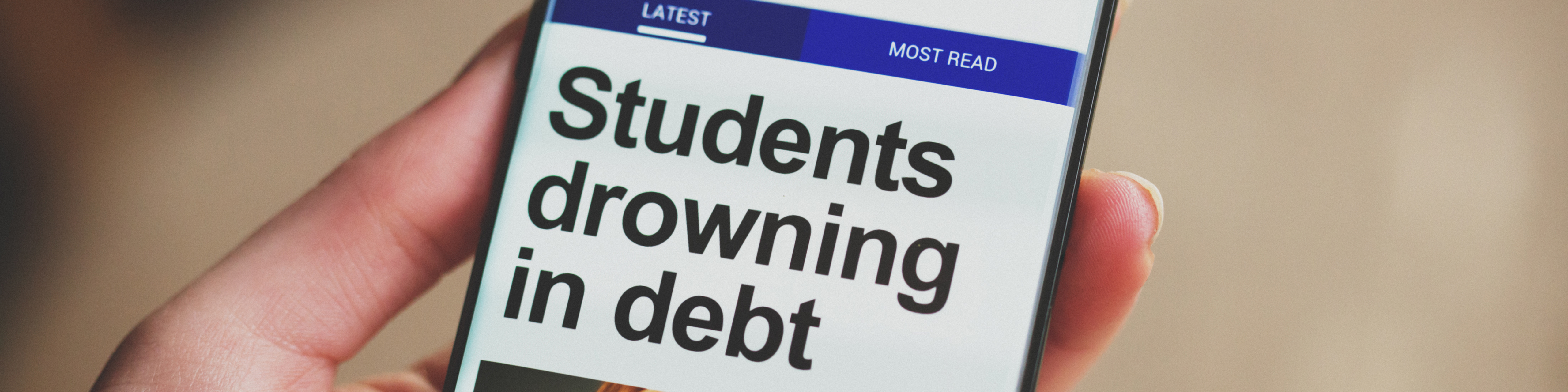 a hand holding a smartphone with the screen showing the headline students drowning in debt