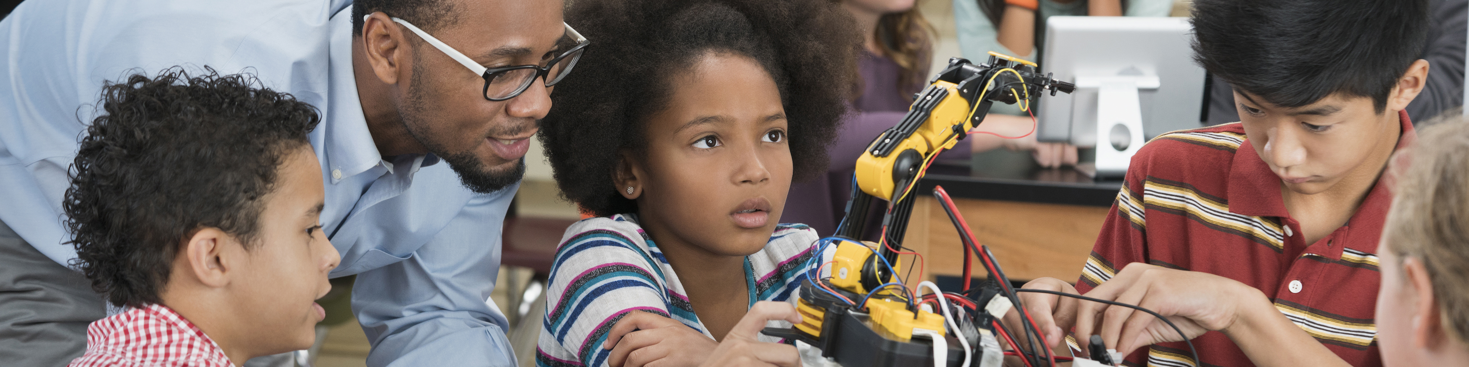 three elementary school students examine a robot with their teacher