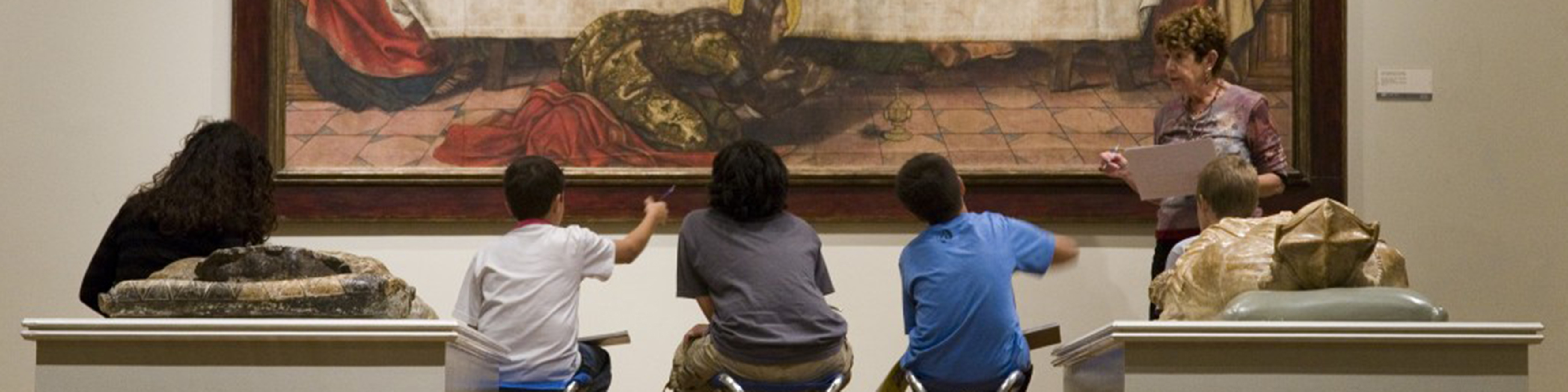 five students sit in front of a painting at the los angeles county museum of art and discuss it with a museum educator
