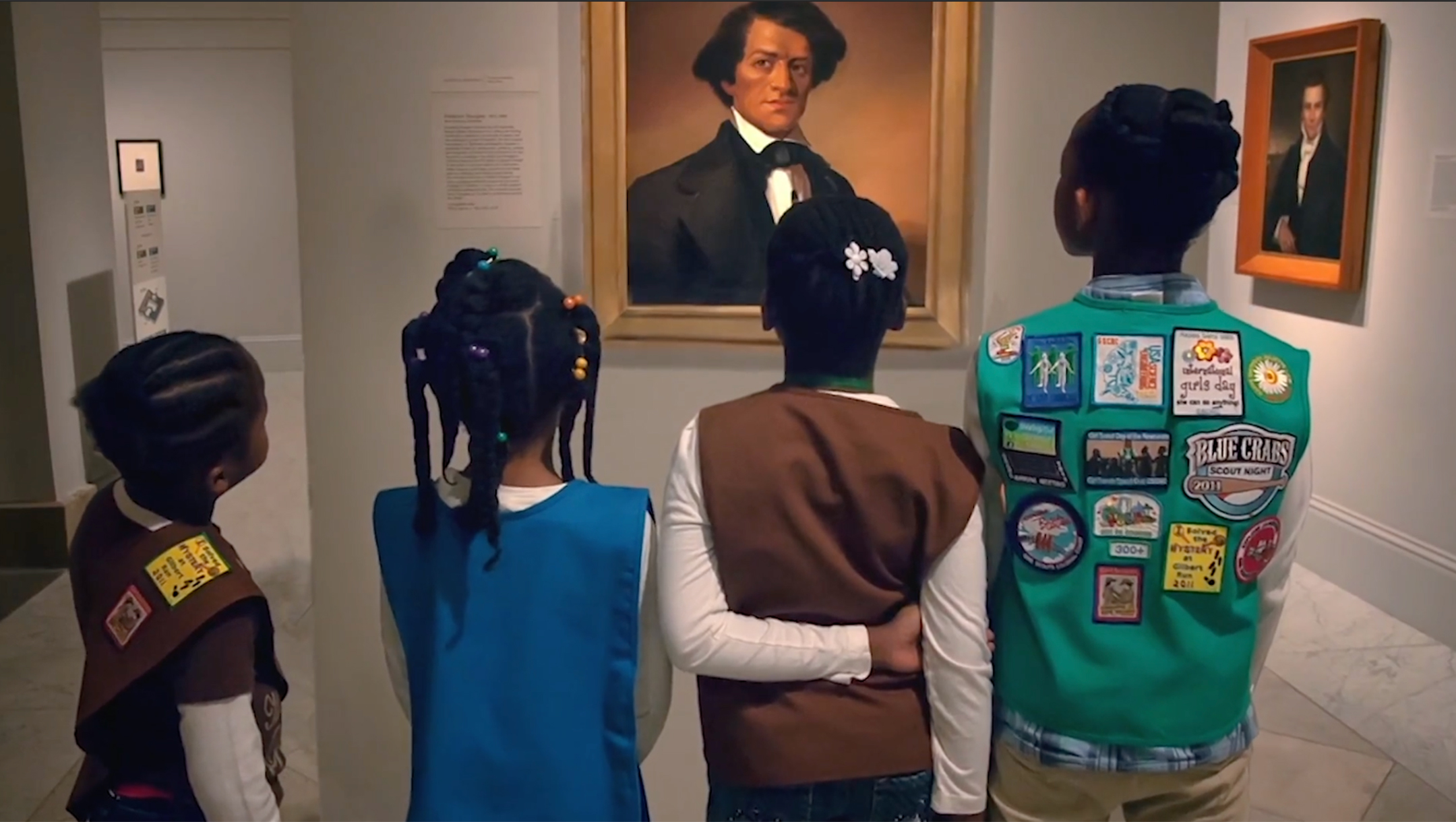 four girl scouts stand in front of a portrait of frederick douglass at the national portrait gallery