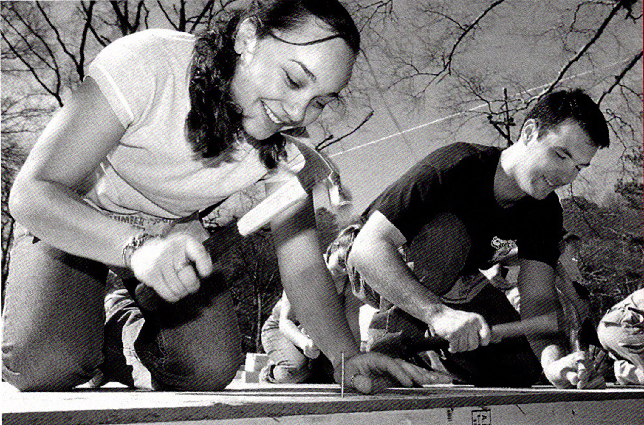 black and white photo of two students pounding nails at a worksite