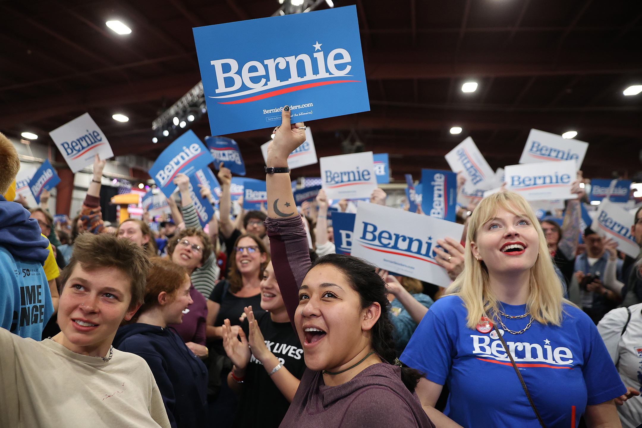 a group of people hold signs supporting bernie sanders at an election night rally