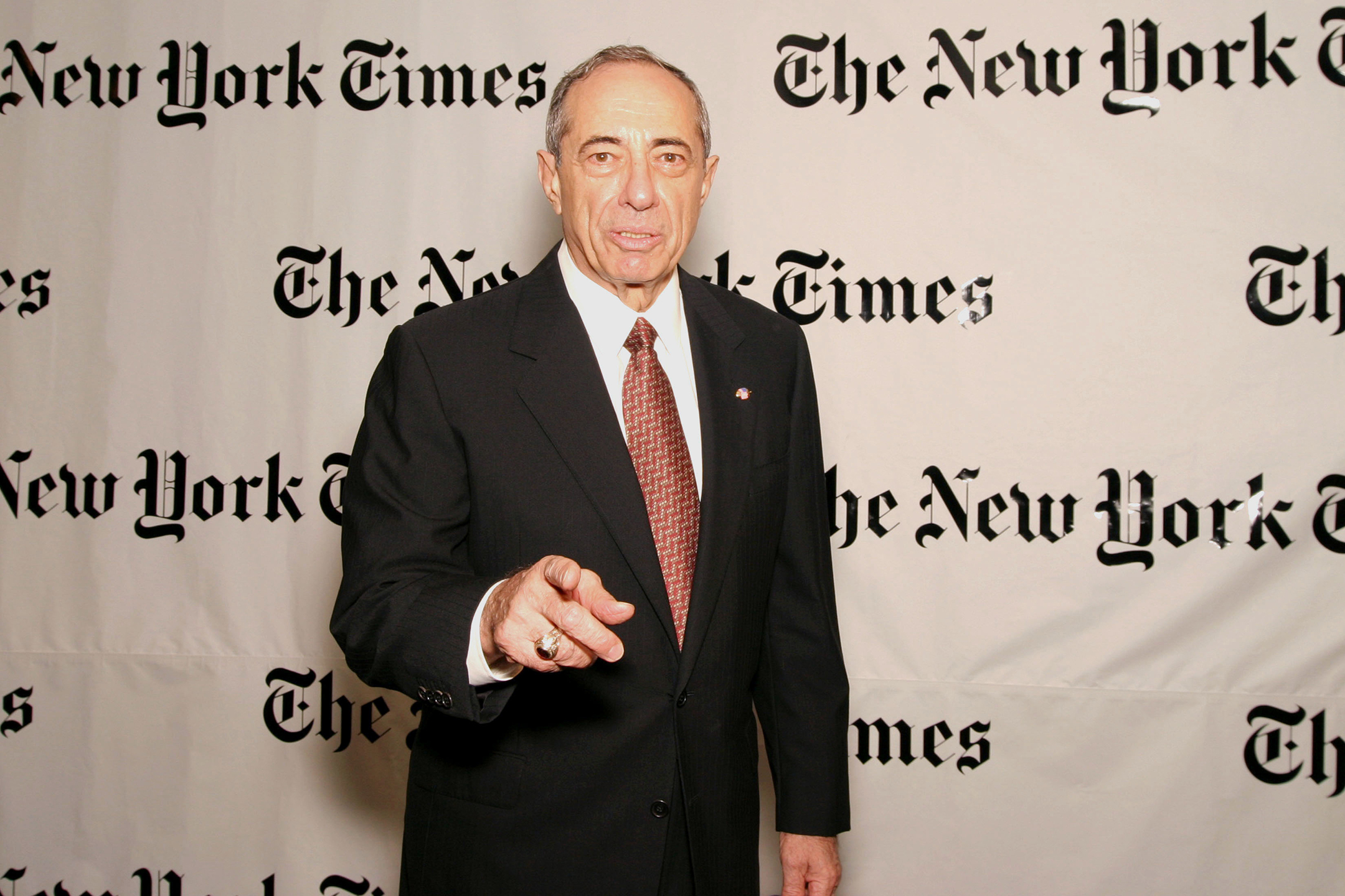 former new york governor mario cuomo points at the camera while standing in front of a new york times banner