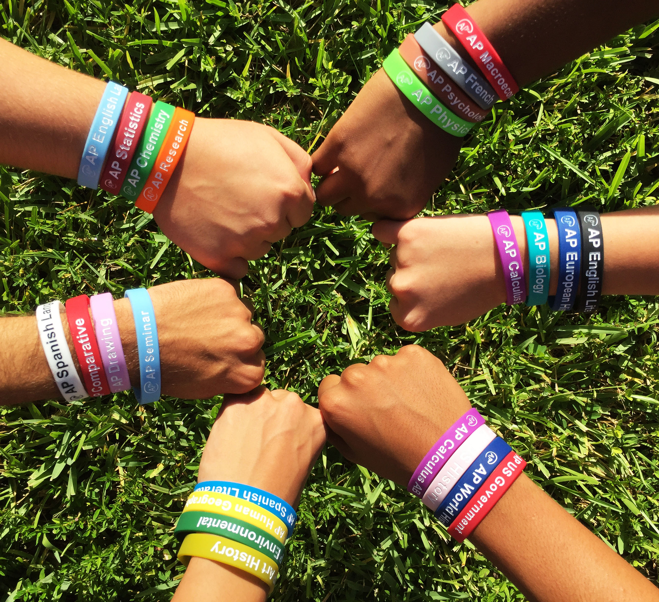 photo of five hands in a circle, fists clenched, with a number of wristbands in different colors on each hand