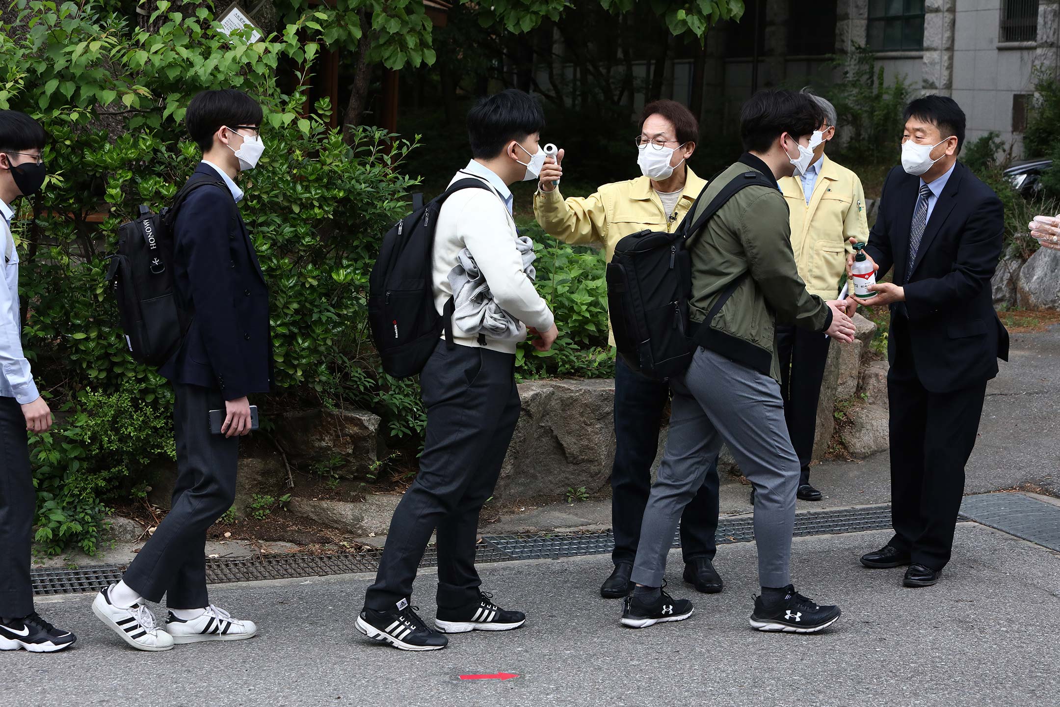 A line of students in South Korea, all wearing masks, get their temperatures taken before entering a reopened school