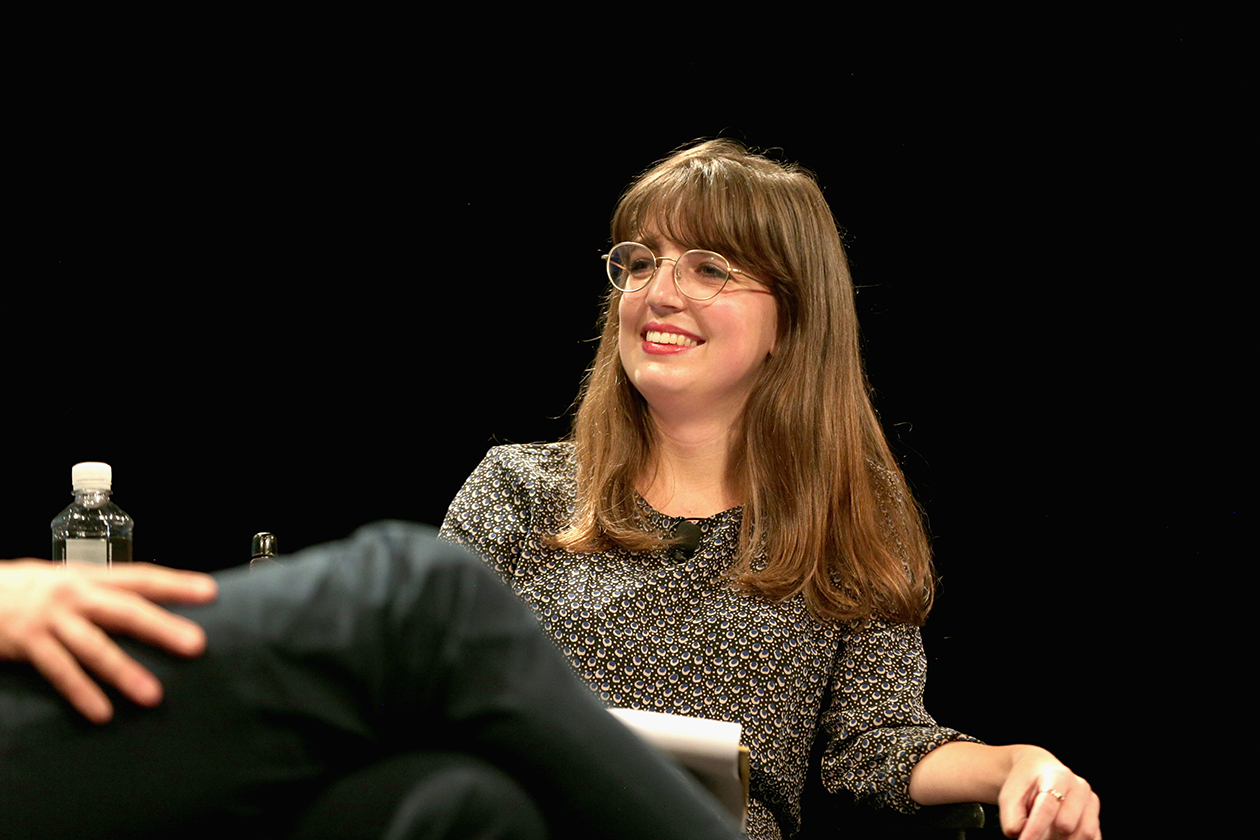 New Yorker cartoon editor Emma Allen smiles while listening to a person she's interviewing onstage 