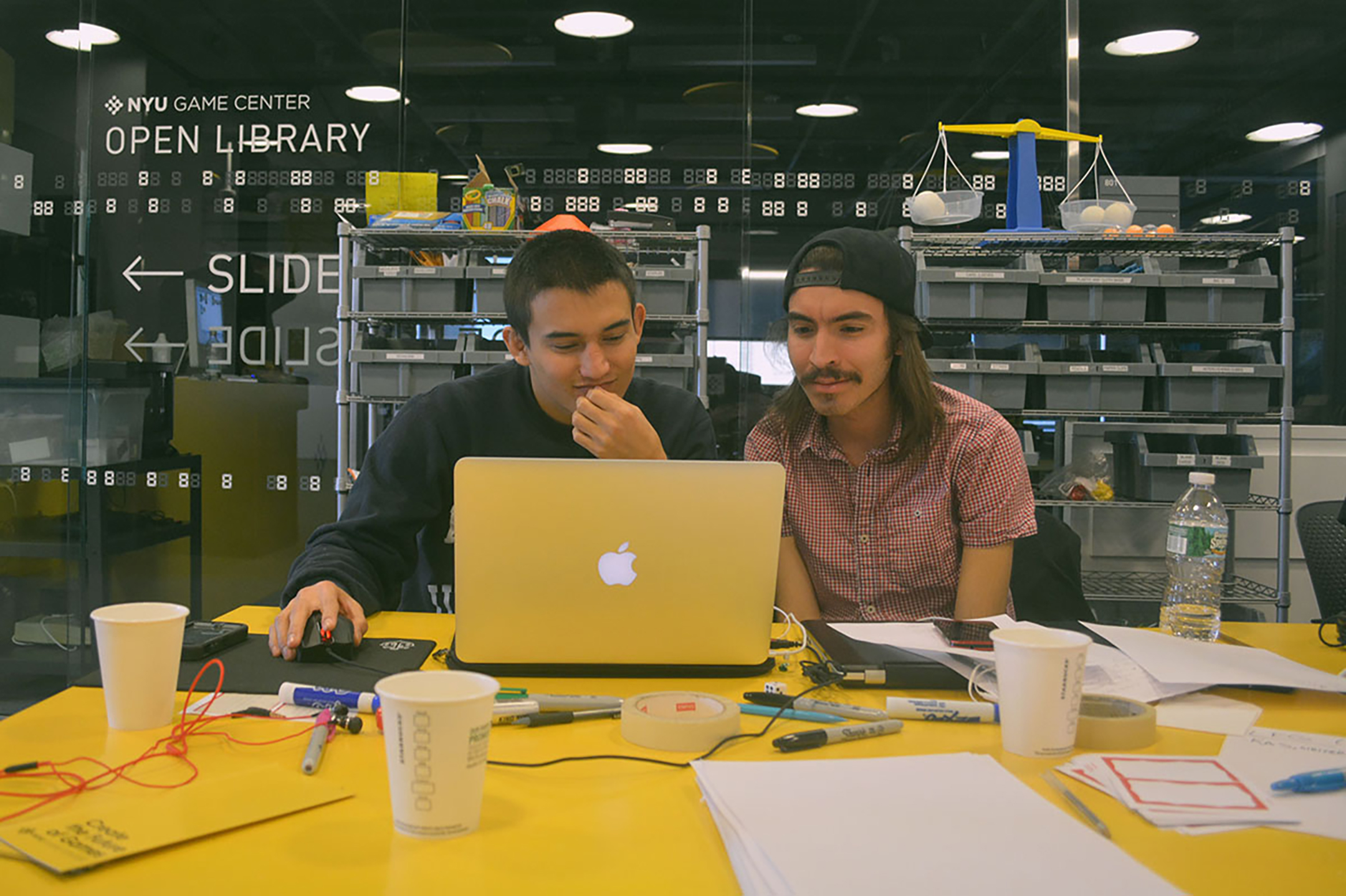 two young men sit in front of a laptop smiling as they work together