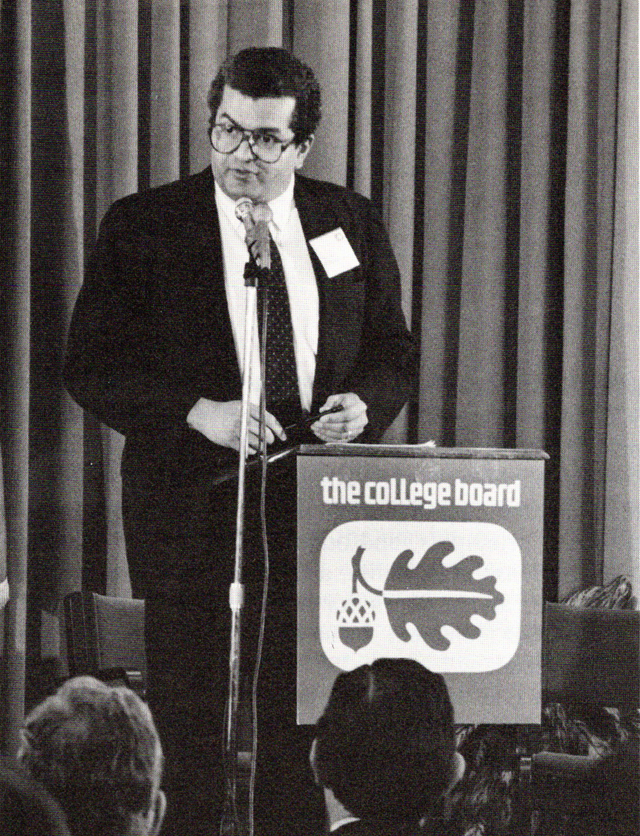 black and white photo of donald stewart, in glasses and a suit, talking to a group from a lectern with a college board logo on the front of it