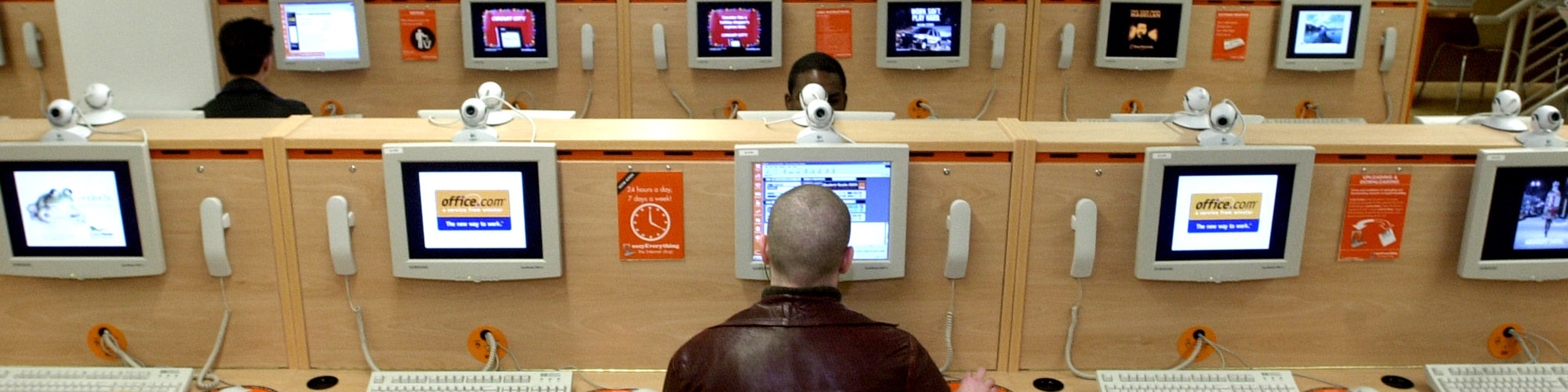 a man sits in front of a computer terminal in an internet cafe