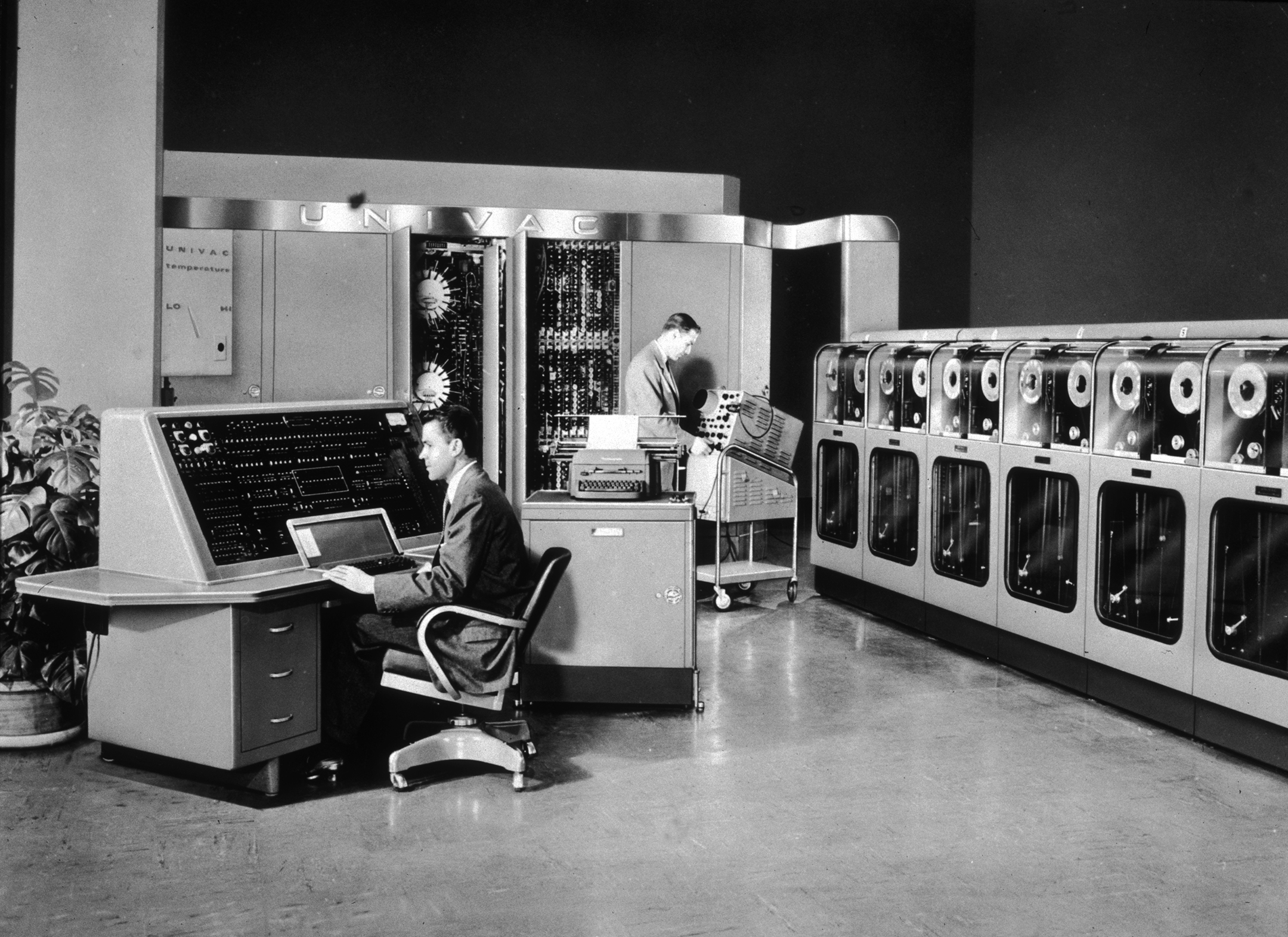 black and white photo of two men in a large room with a very large old computer system