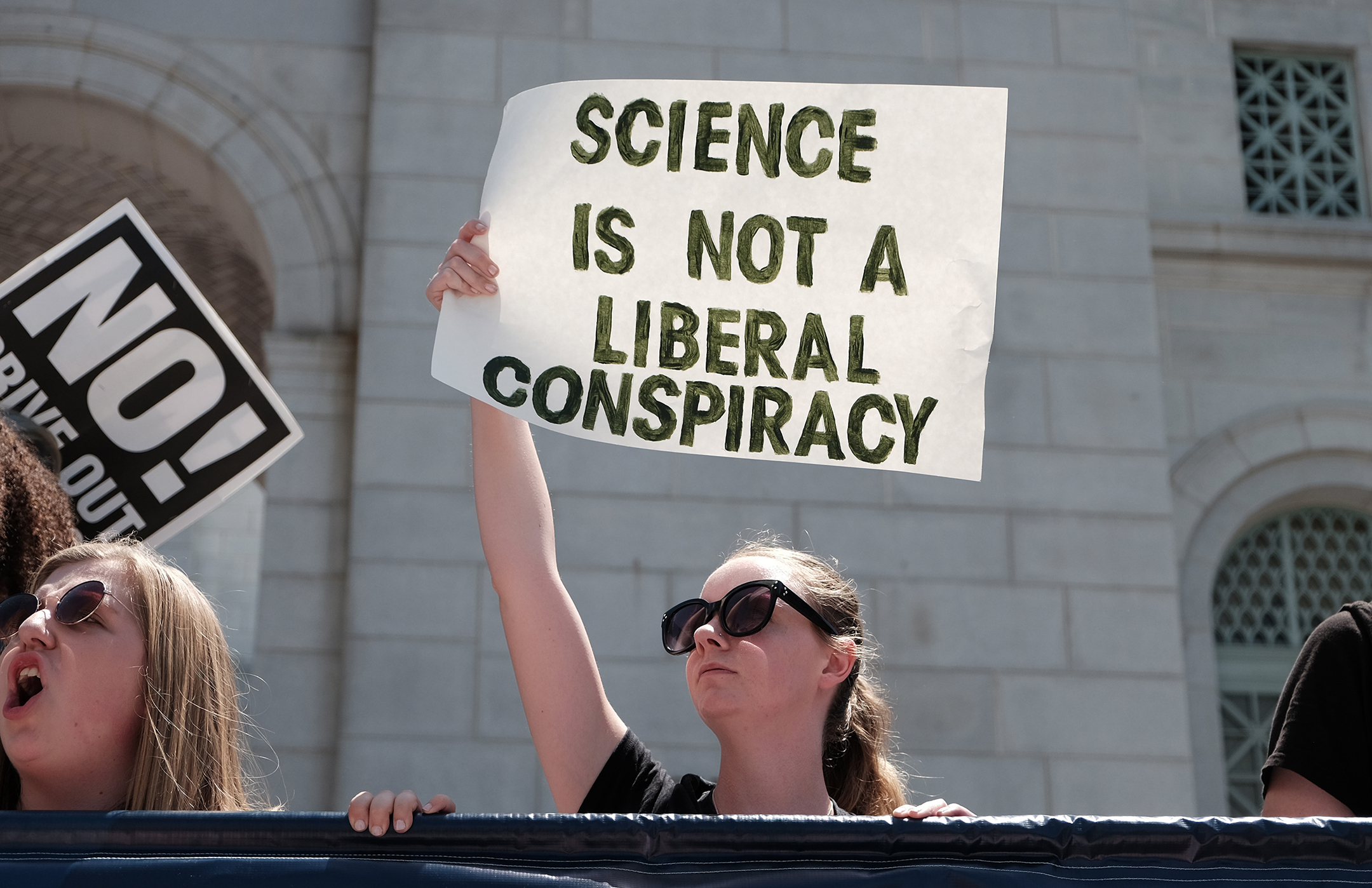 A young woman holds up a sign that reads science is not a liberal conspiracy
