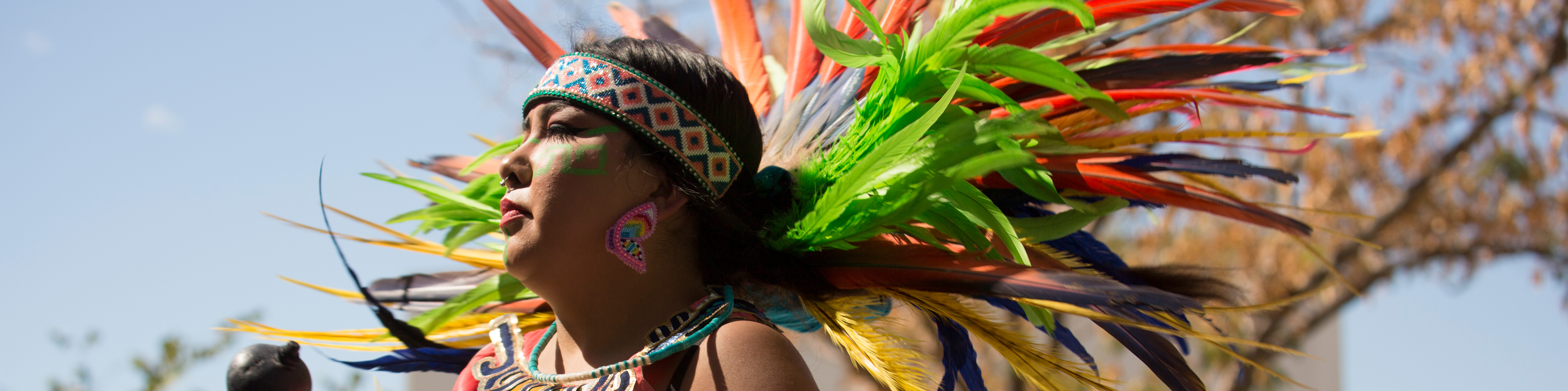 A Native American woman in a colorful headdress looks left during a celebration