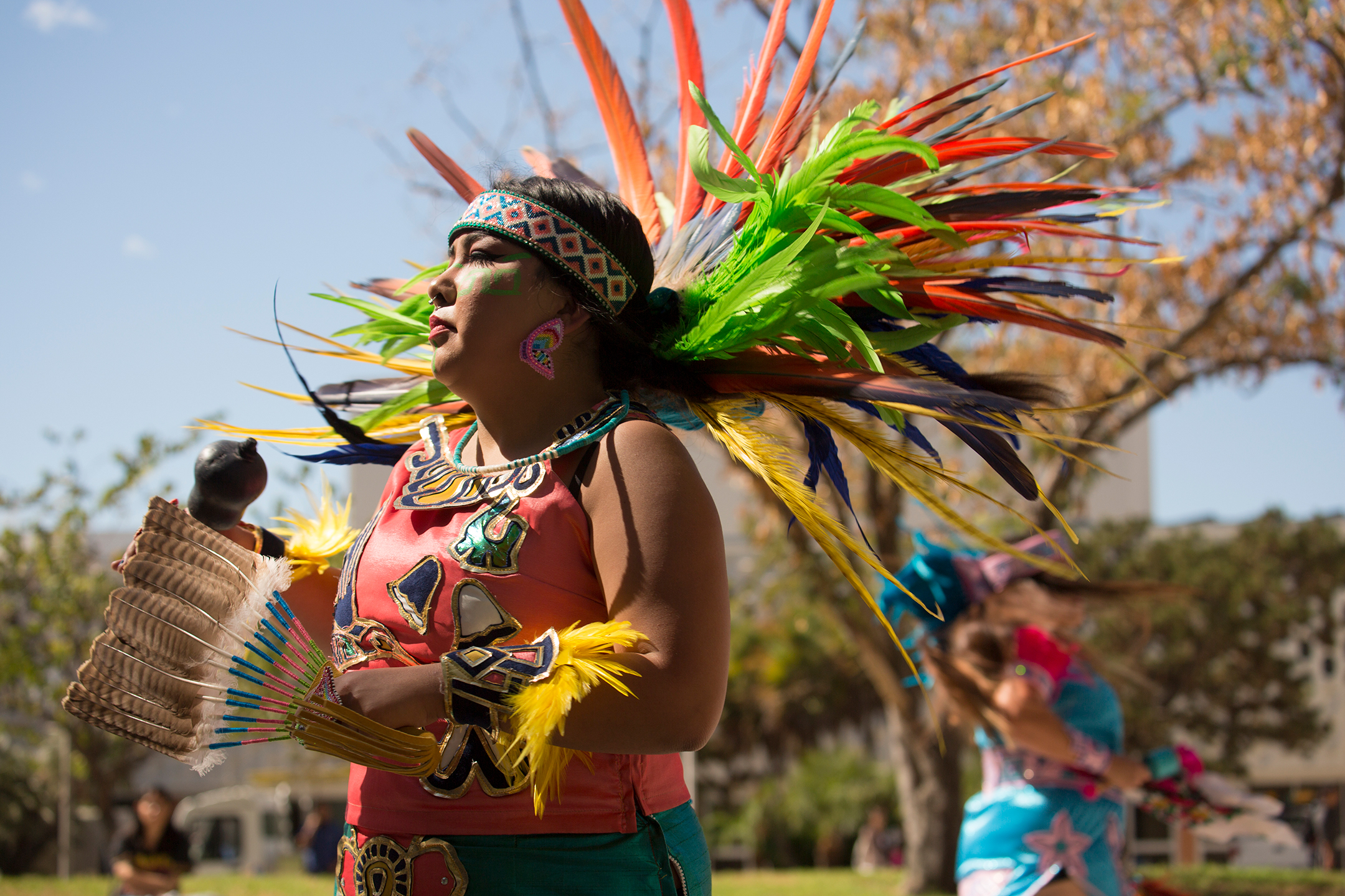 A Native American woman in a colorful headdress looks left during a celebration