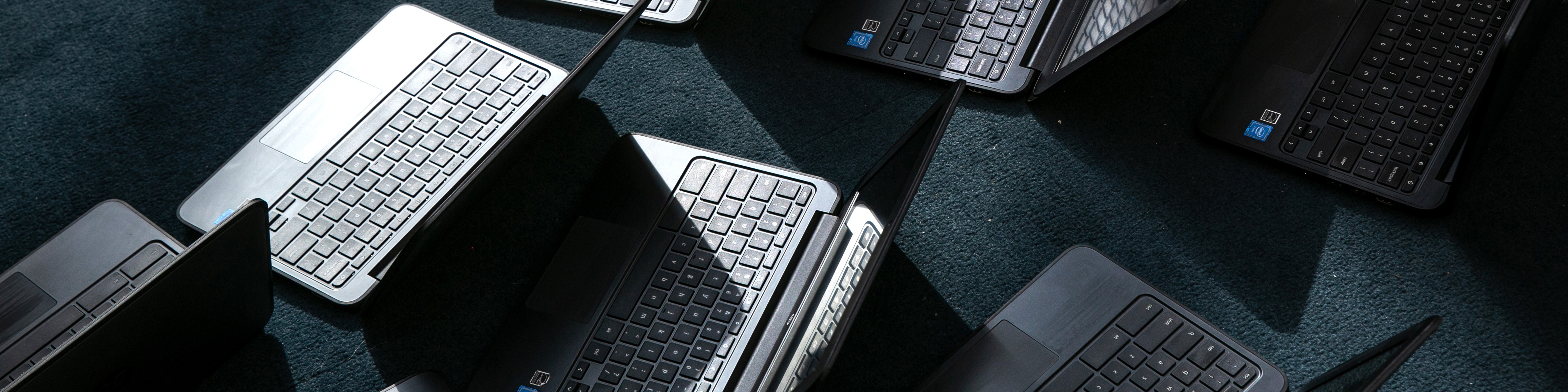 A photo from above of a group of black laptops, open and sitting on a carpeted floor