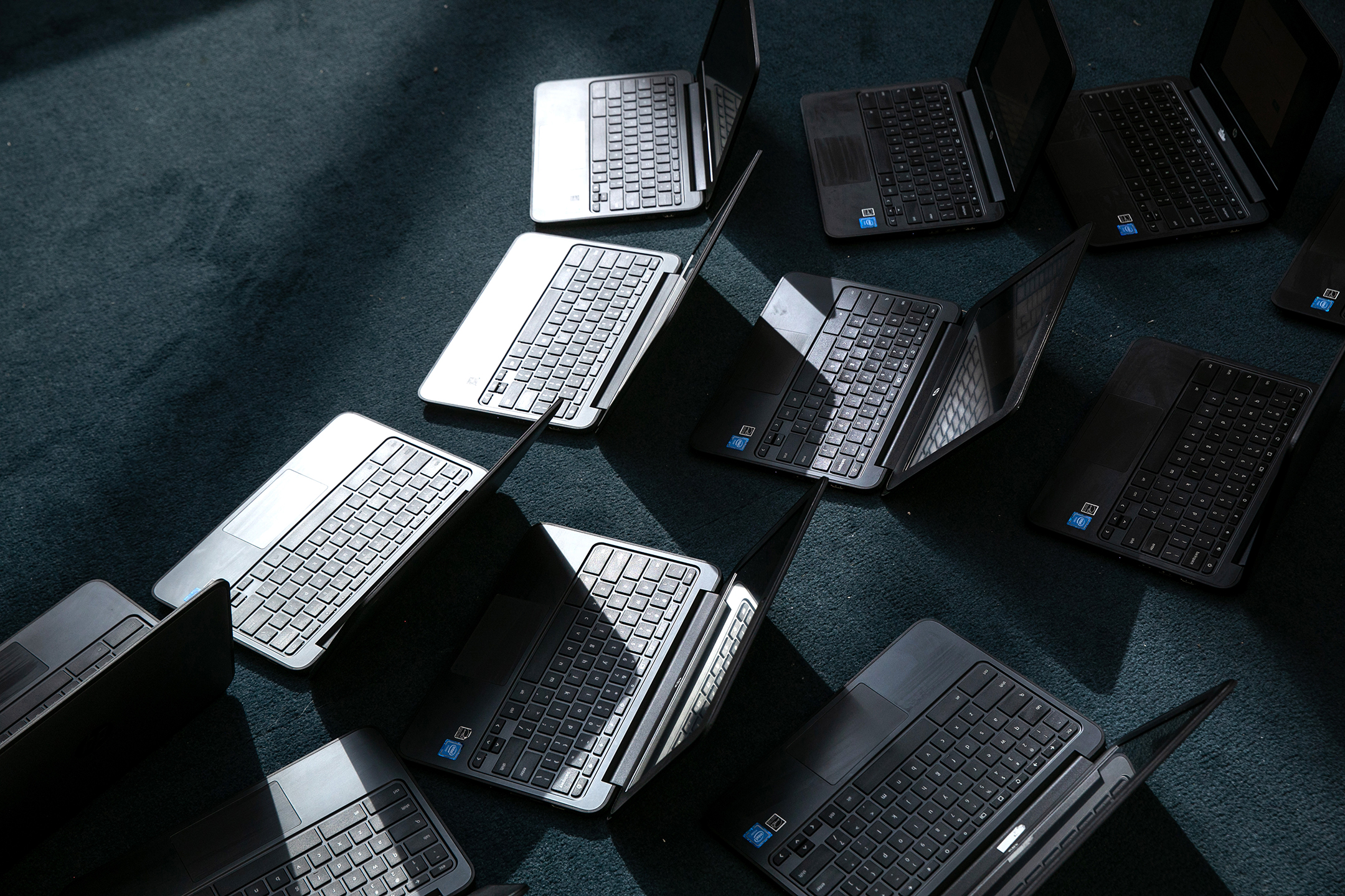 A photo from above of a group of black laptops, open and sitting on a carpeted floor