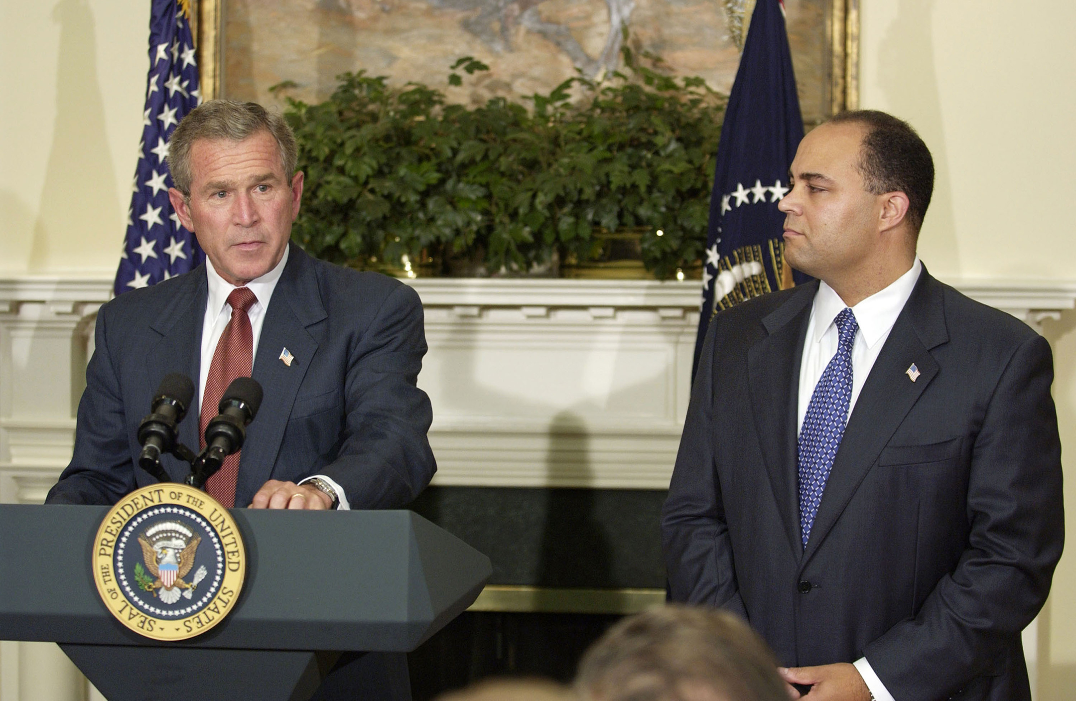 President George W. Bush, on the left, stands at a podium while Michael Powell, on the right, listens