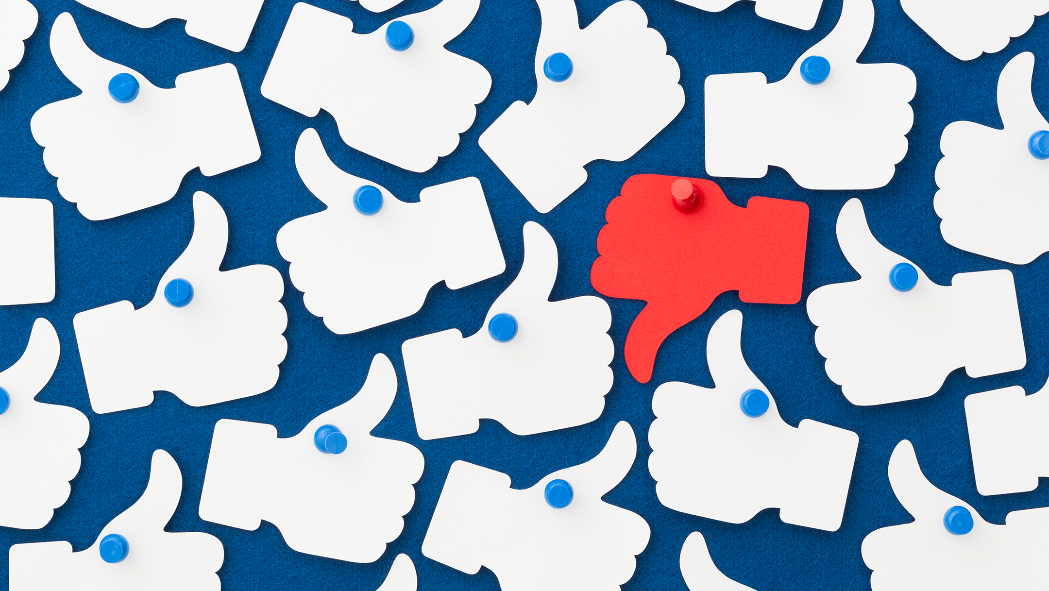 grouping of multiple white facebook thumbs up icons with one red thumbs down icon, all against a blue background