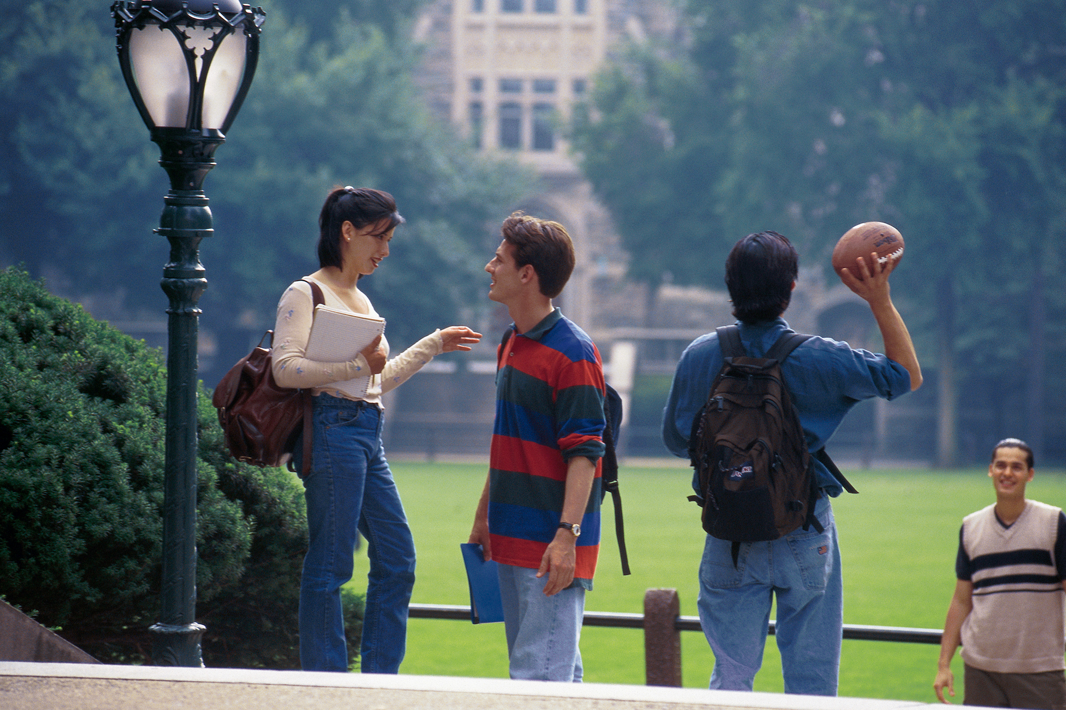 Four college students on a campus, two talking to each other, the other two tossing a football
