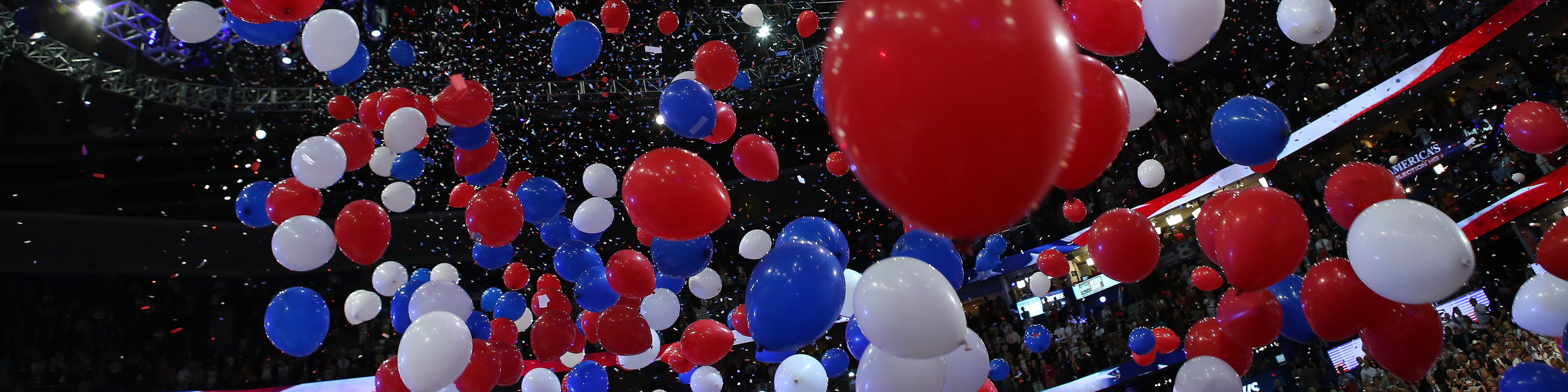 Photograph from a political convention showing red white and blue balloons falling from the ceiling of the arena