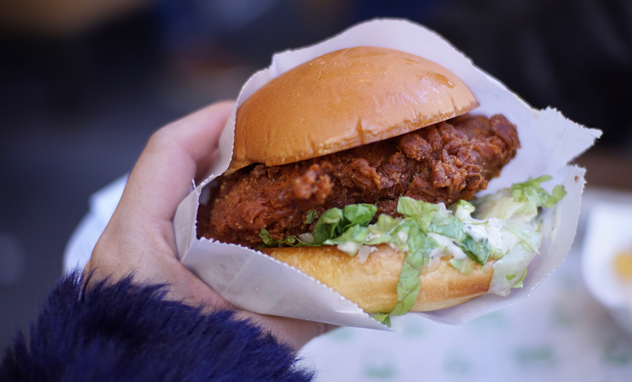 A female hand holding a fried chicken sandwich