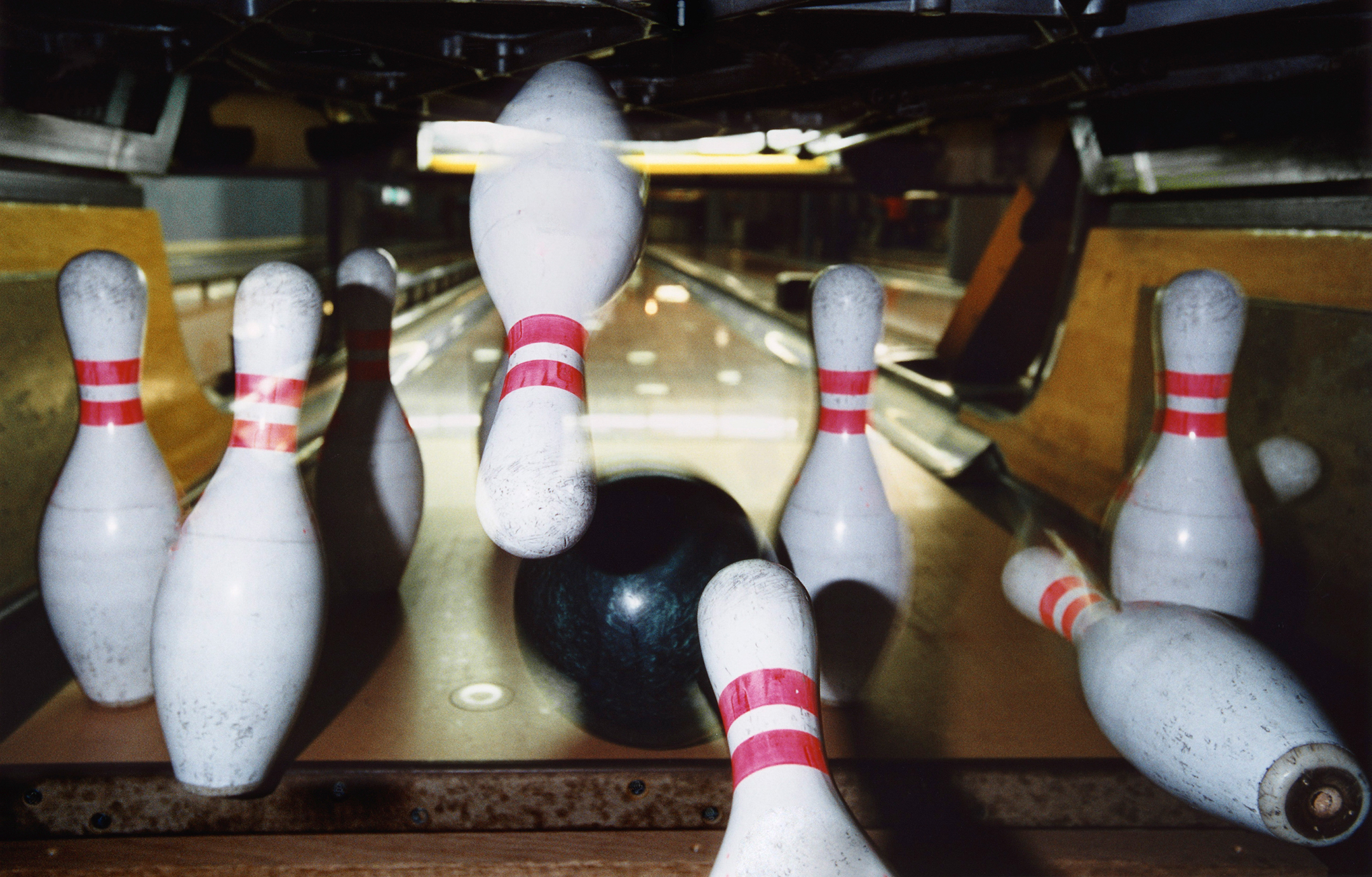 A set of bowling pins seen from behind as a bowling ball knocks them down
