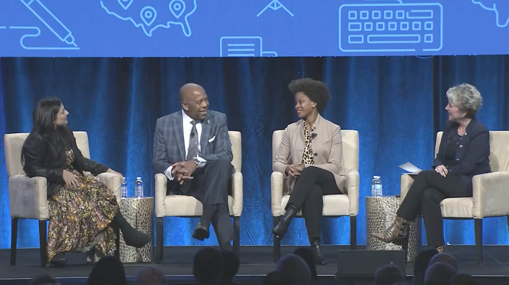 Screenshot of a video showing four panelists sitting on a stage