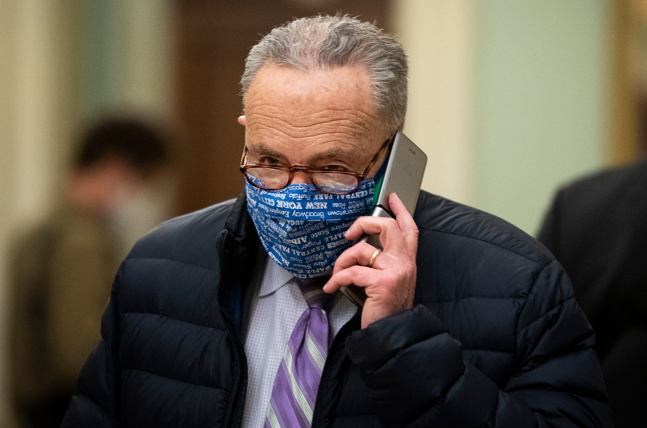 Chuck Schumer wearing a face mask and puffy coat while talking on his cell phone
