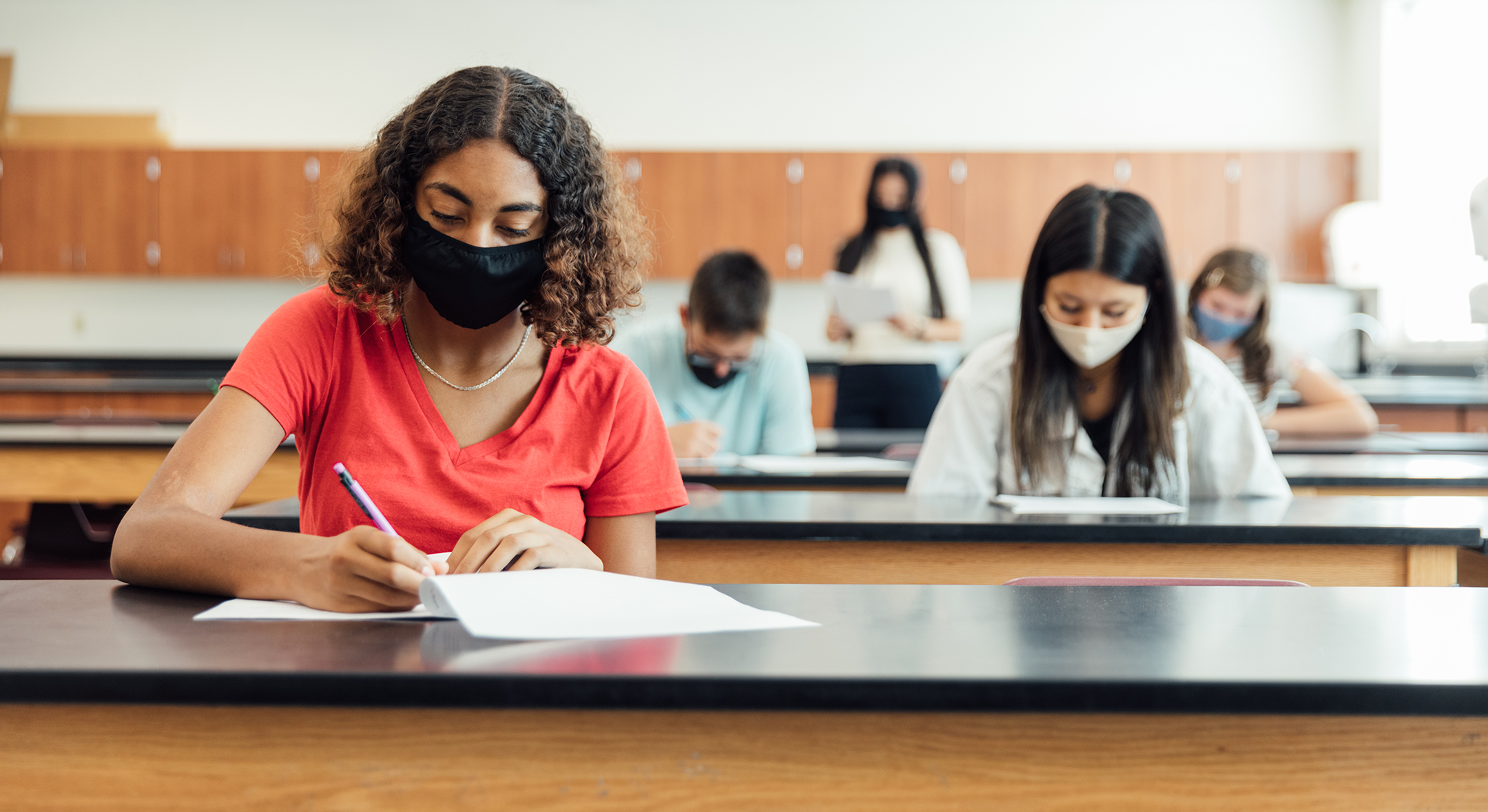Students, socially distanced and wearing face masks, take a test in a science lab