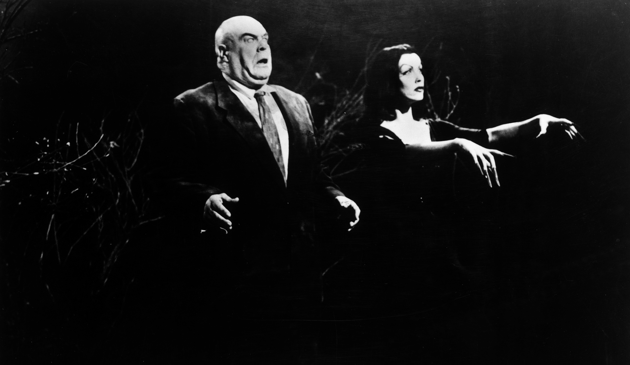 Black and white still image from plan nine from outer space depicting a bald man and a lithe woman walking like zombies