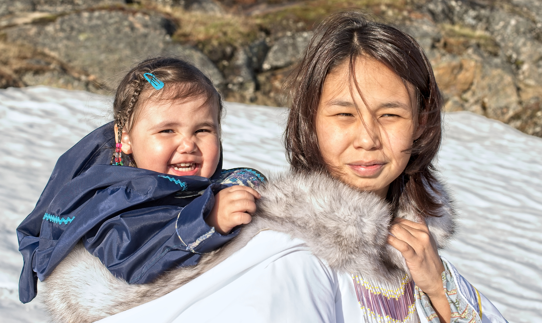 Toddler smiling while wearing traditional Inuit clothing and being carried on its mom's back