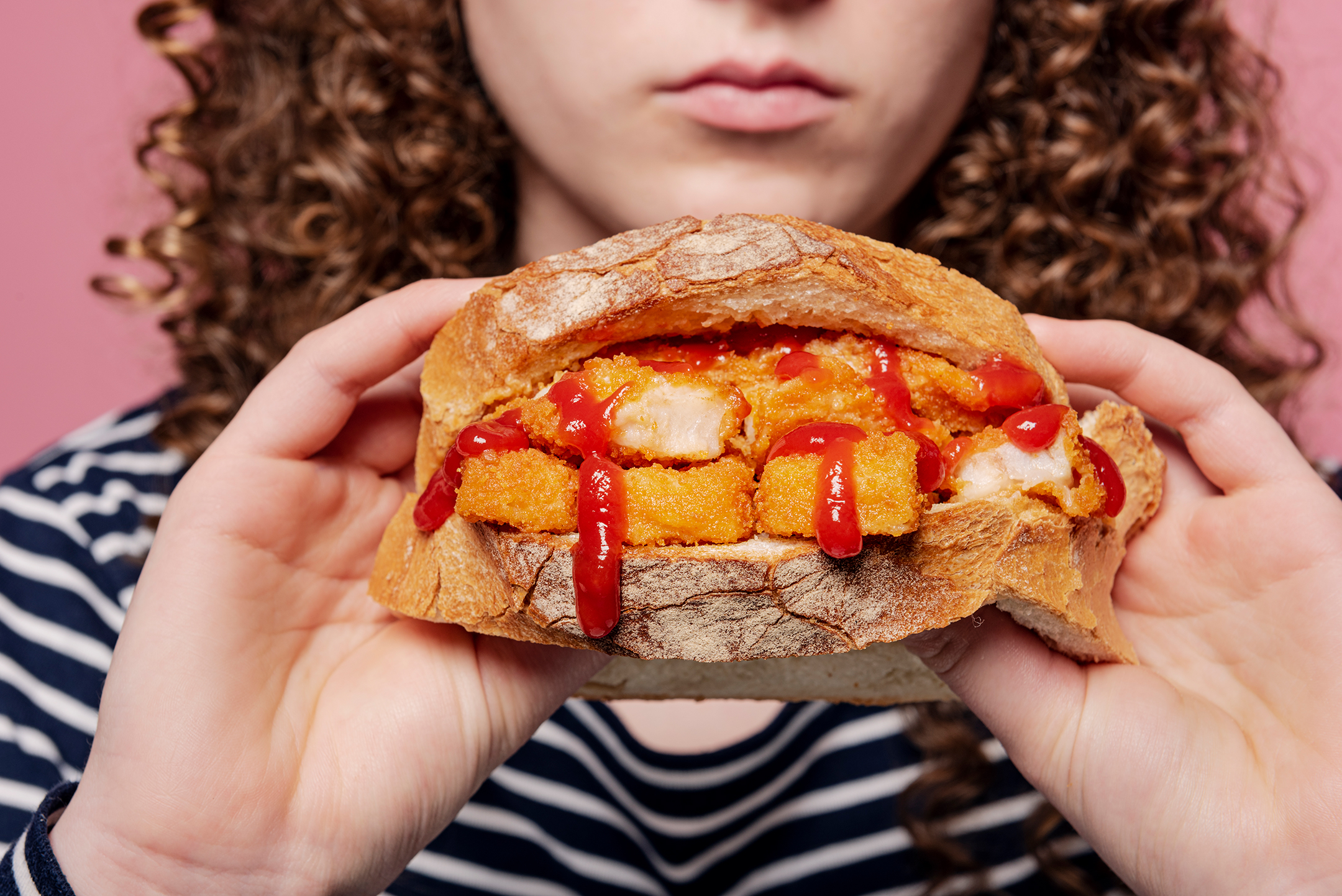 Young woman holding a Fish Finger Sandwich of deep fried fish sticks between two slices of white bread oozing with tomato ketchup