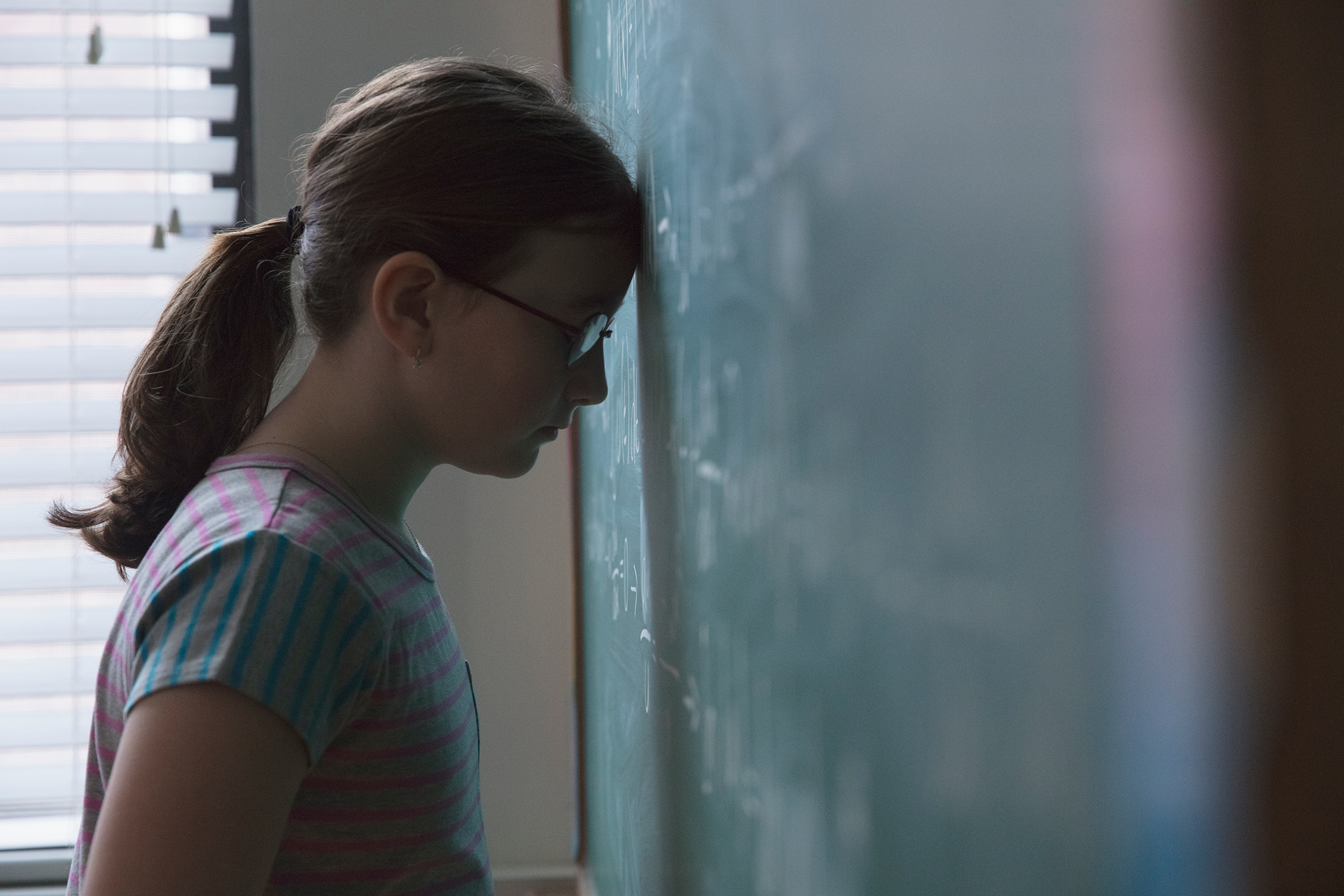 Frustrated schoolgirl with her head against a chalkboard