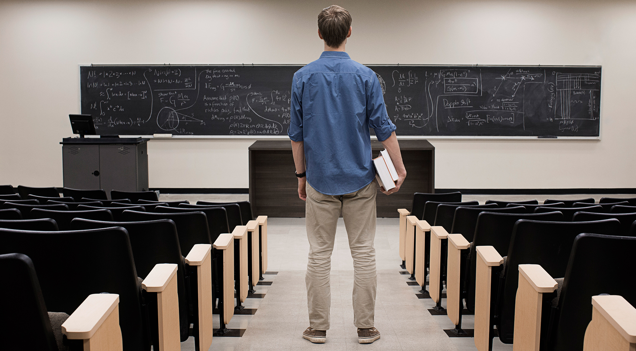 Male student, seen from behind, stares at a long blackboard with math equations written on it.