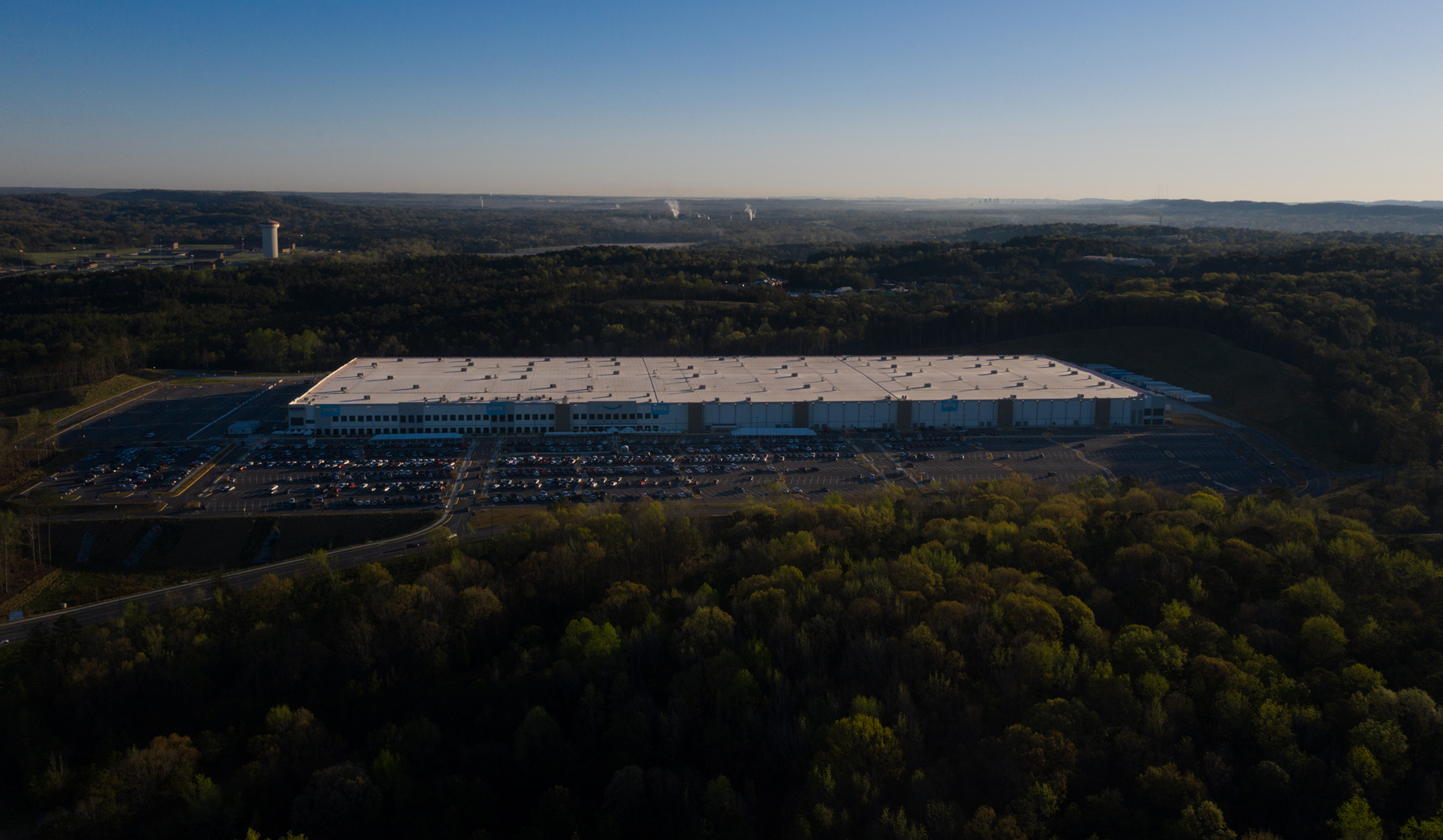 View of a large Amazon warehouse seen from the air, set in a rural landscape of forests and empty spaces