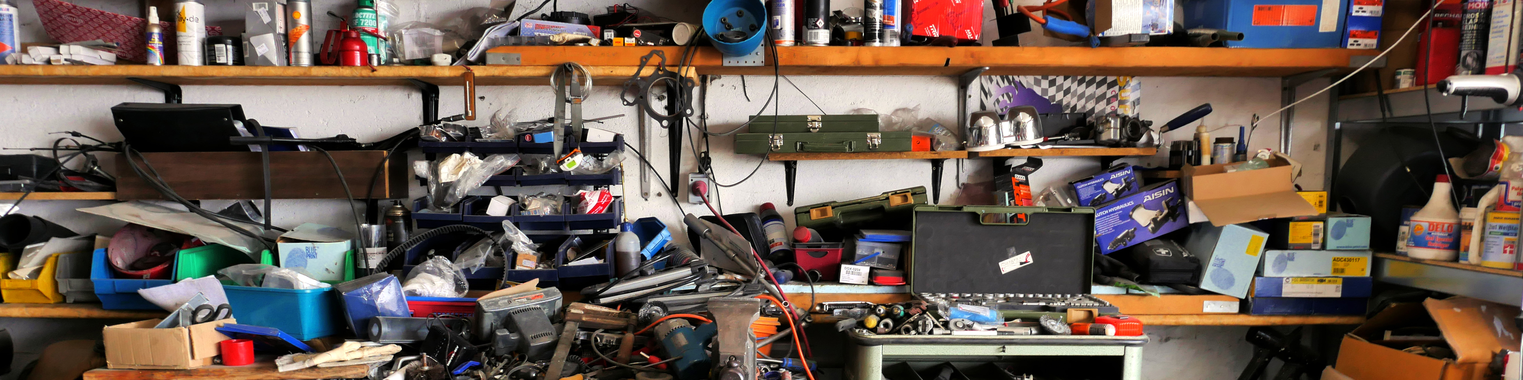 Private garage interior, very untidy. A workbench is drowned under a wild mix of tools, cans, boxes and what not. Nowhere to stand, let alone move. 