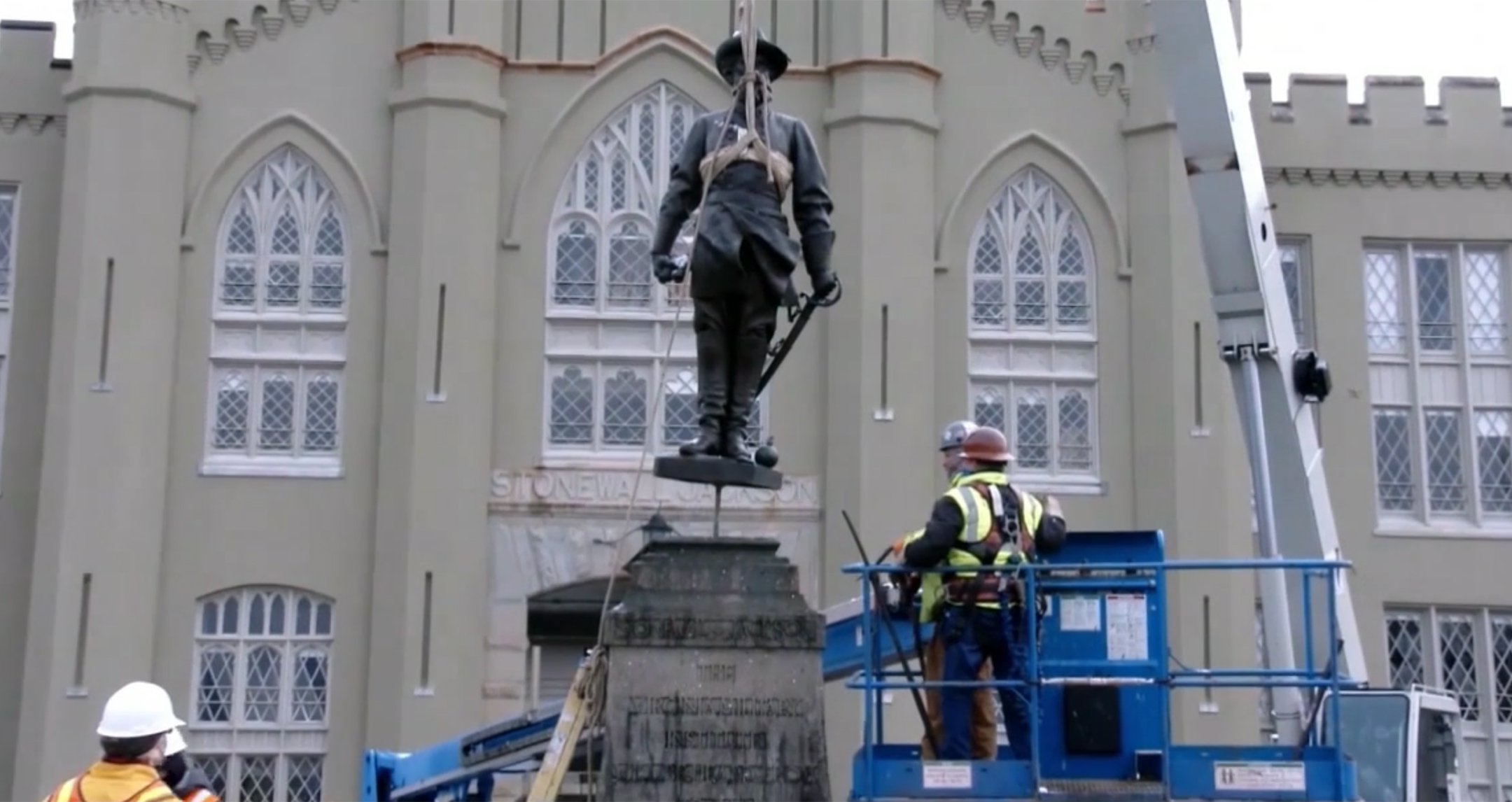 Statue being lifted off its base by workmen and a crane