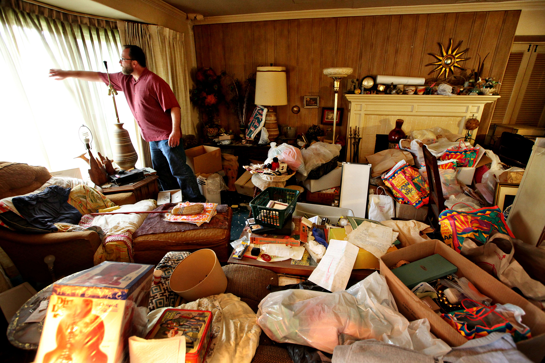 Photo of a living room cluttered with stuff, with Greg Martin looking out the window on the left