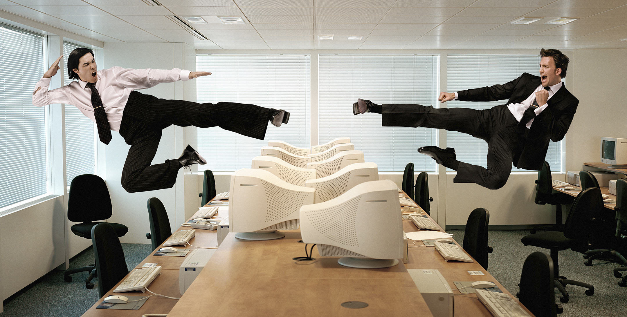 Two men kicking in mid-air across row of computers 