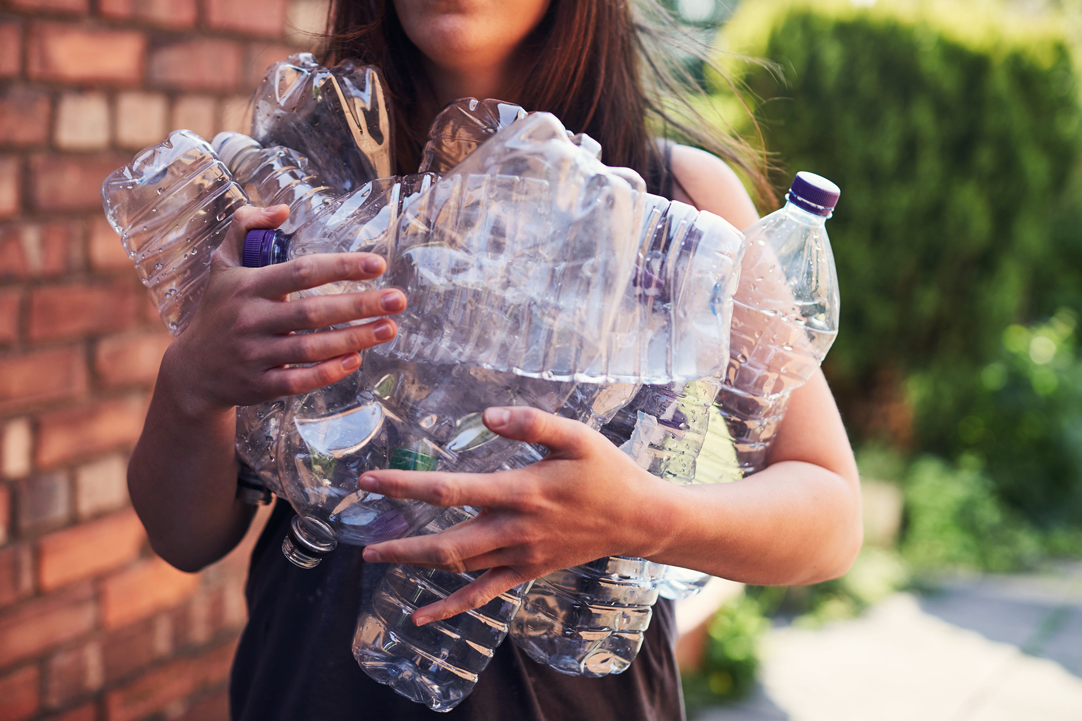 Photo of a young woman holding a box overflowing with empty plastic water bottles