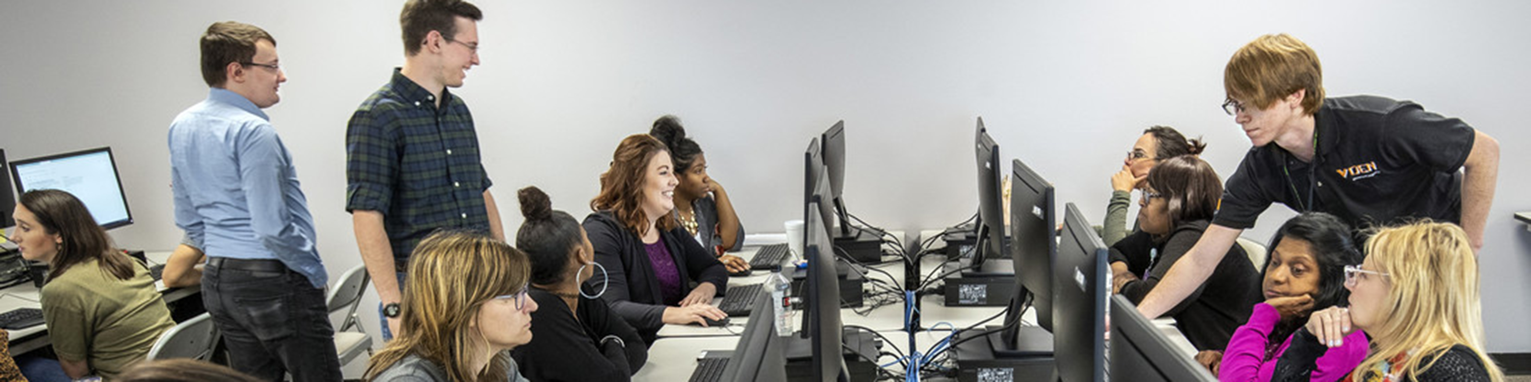 College students help adult learners sitting at a bank of computers